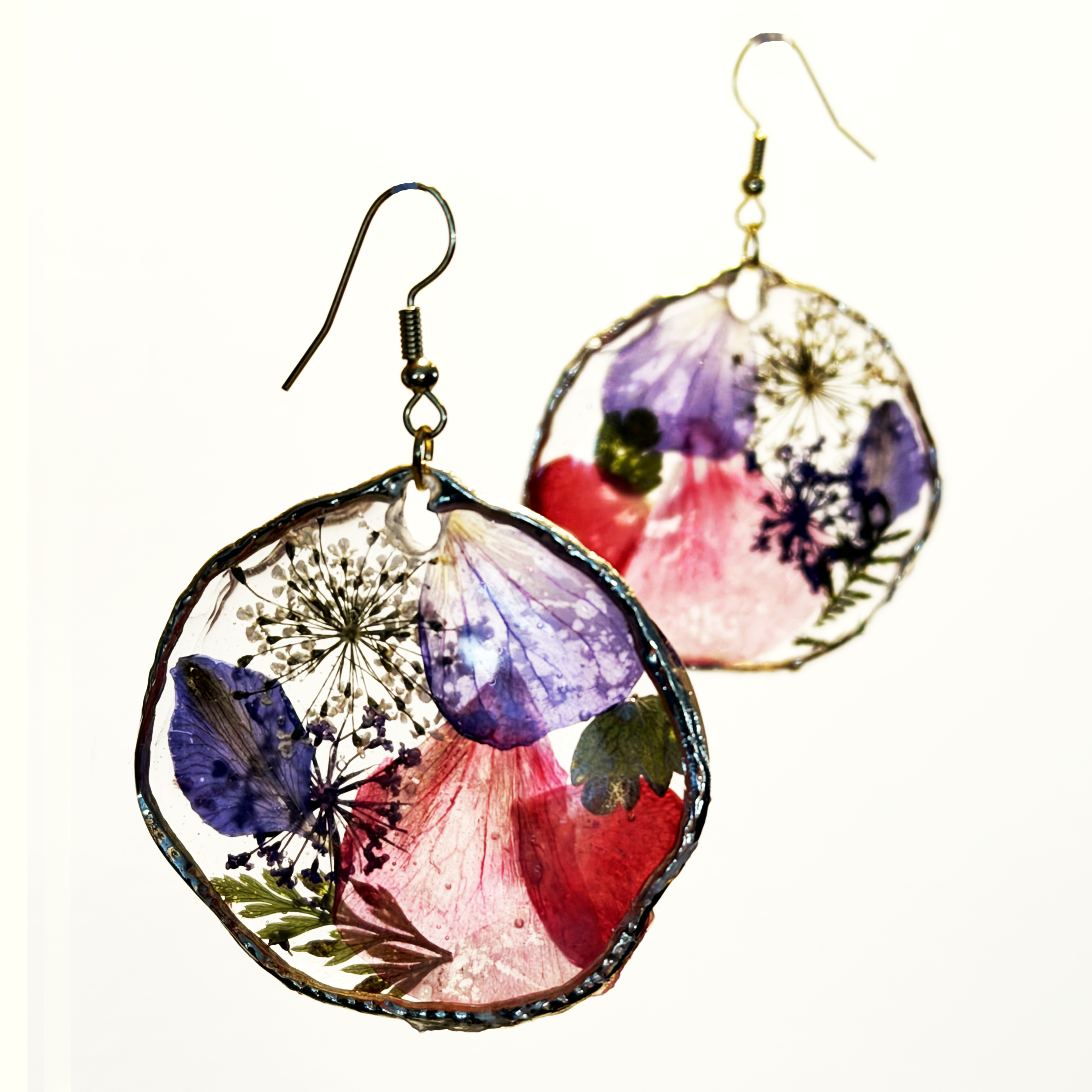 Pumpkin-shaped earrings made of resin with pressed flowers and leaves inside, hanging on metal hooks.