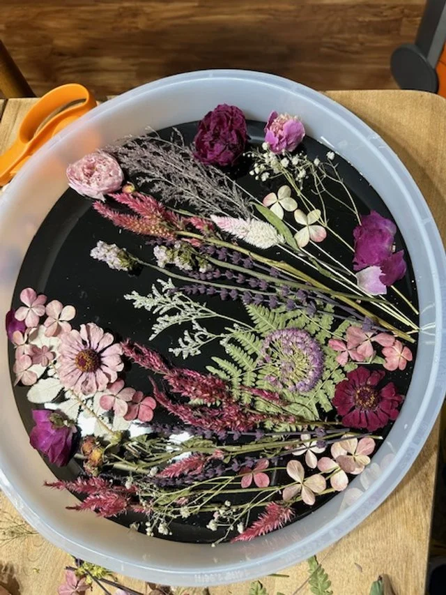 A large white basin filled with water and floating dried flowers and plants in shades of pink, purple, white, and green.
