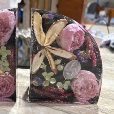 A piece of transparent resin with embedded dried pink flowers, lemon slices, green berries, and small purple and white flowers.
