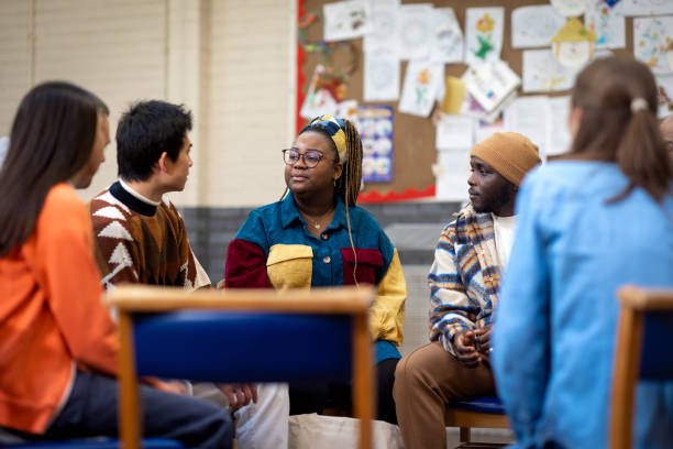 A diverse group of young adults sitting in a circle in a classroom, engaging in a discussion.