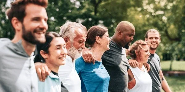 Group of diverse people standing outdoors with arms around each other's shoulders, smiling