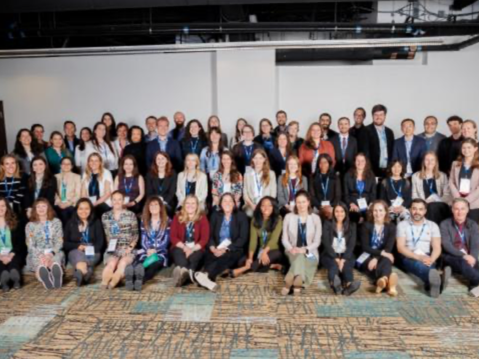 A large group of professionally dressed people gathered in an indoor conference room posing for a group photo.