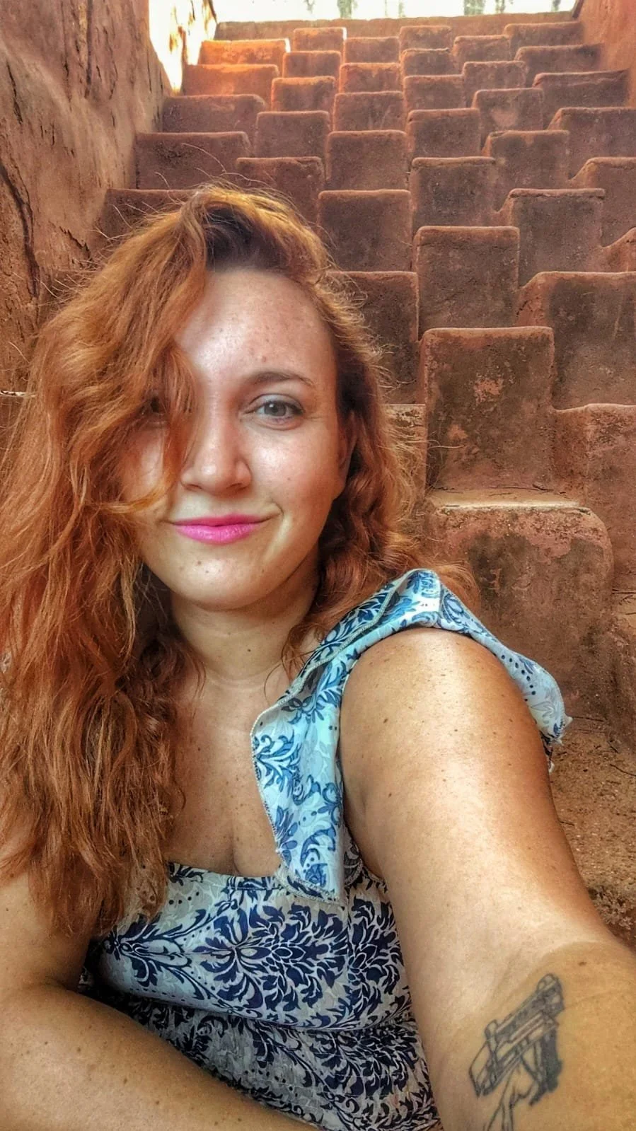 A woman taking a selfie in front of an ancient stone amphitheater with terraced seating.