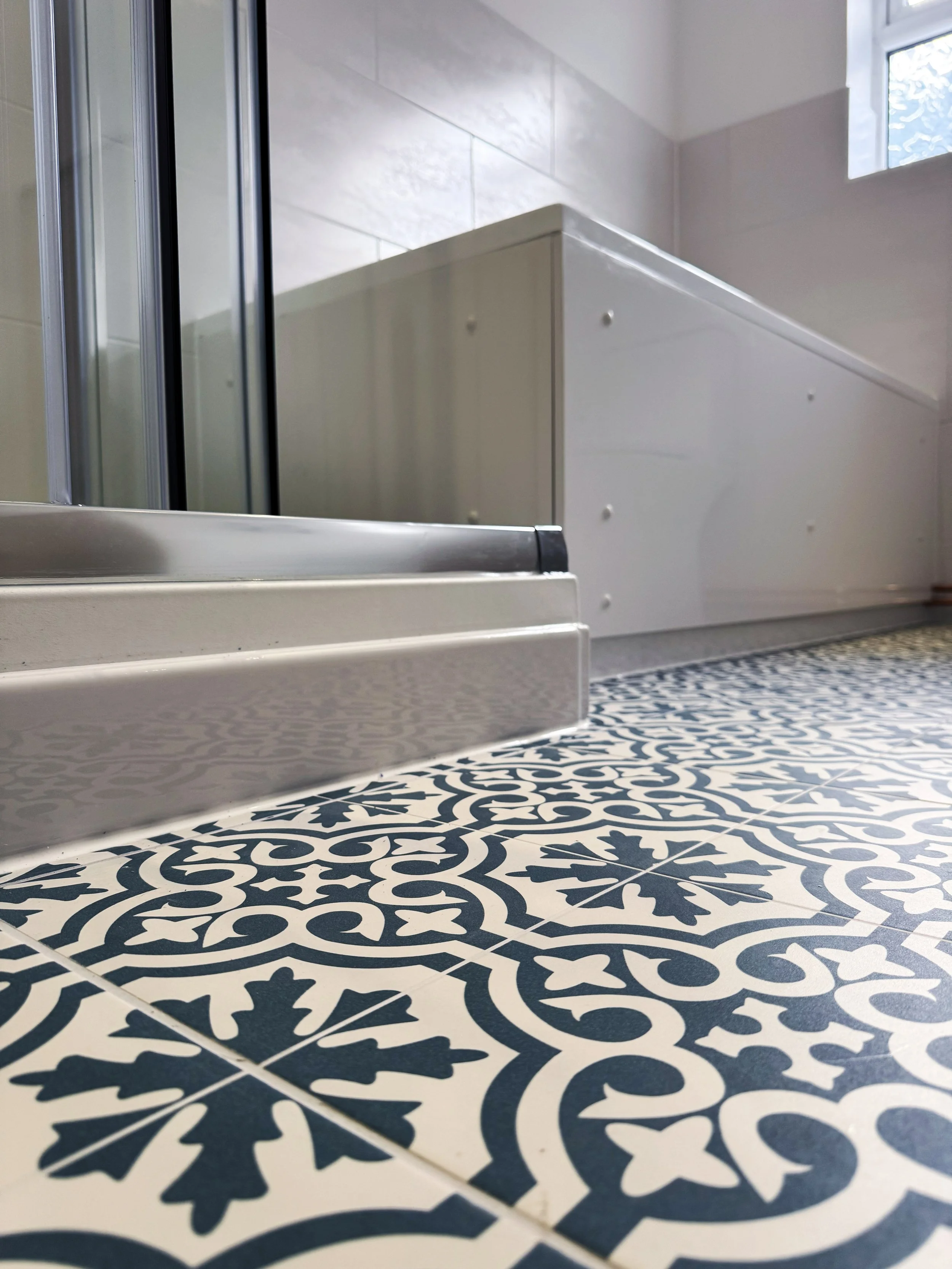 Close-up of patterned bathroom floor with shower base and white cabinets in the background.
