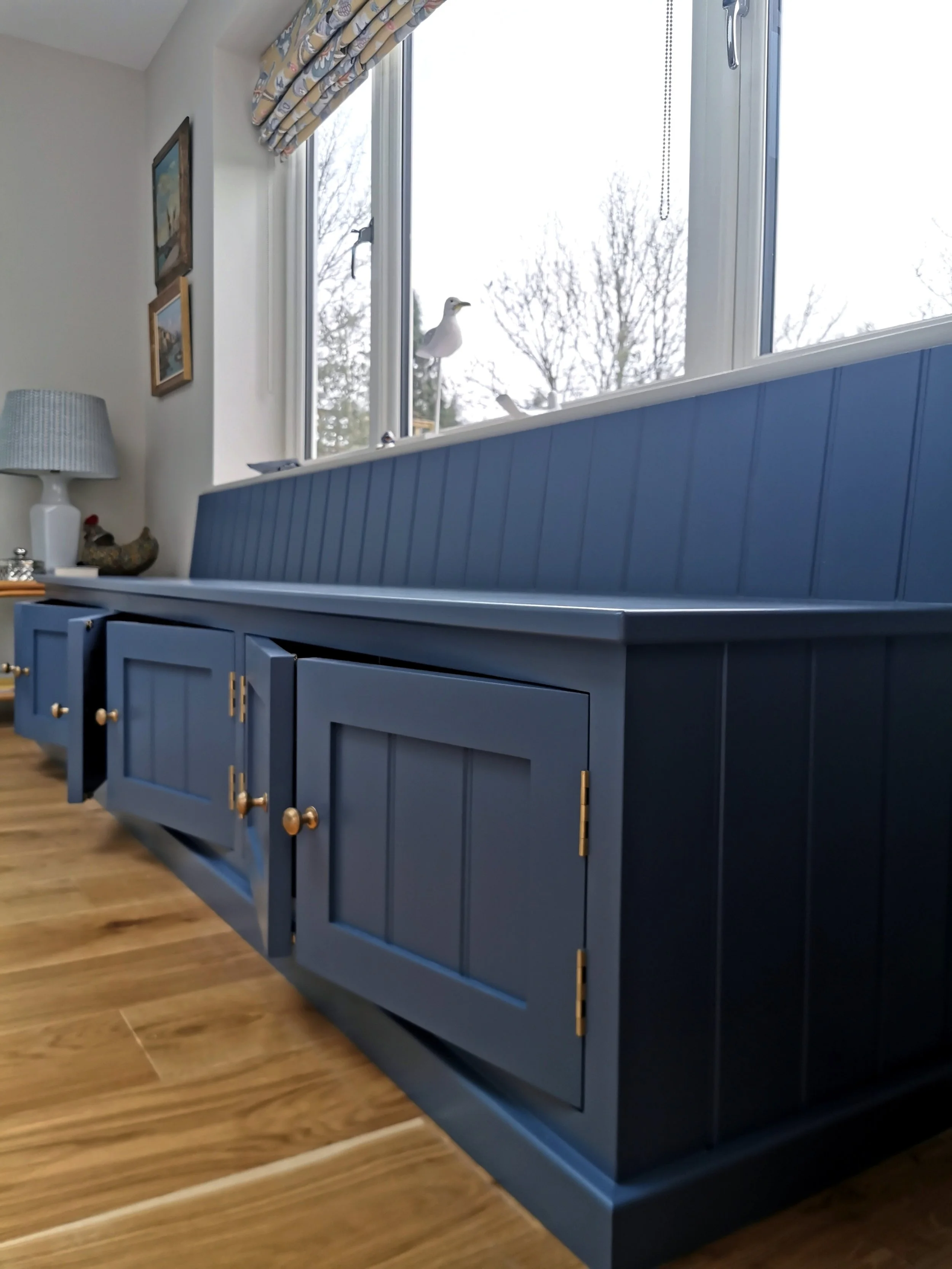 Blue wooden sideboard with gold hardware in a room with a window and framed pictures on the wall.
