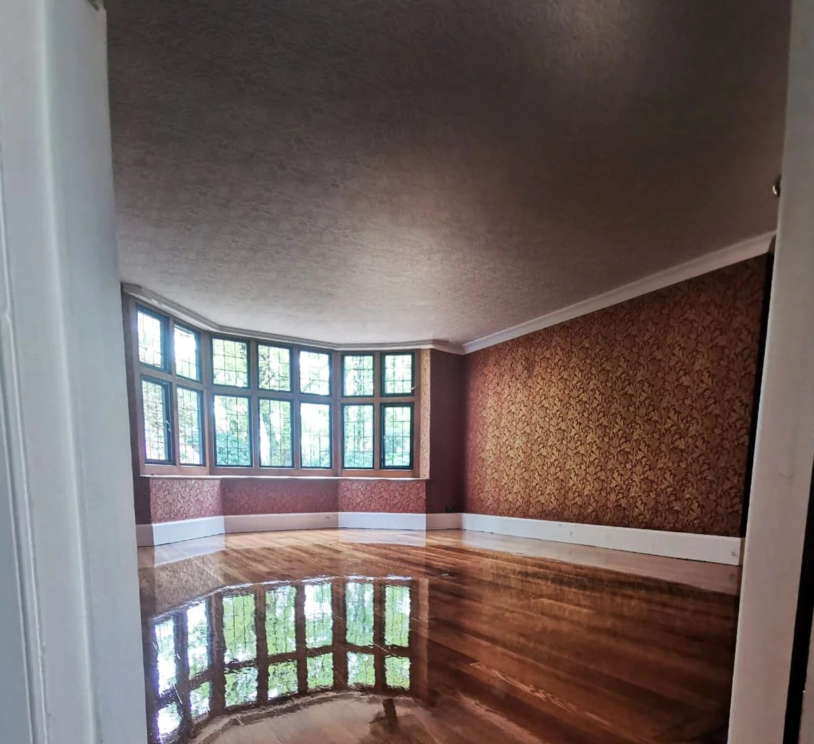 Empty room with wood flooring, large bay window, and floral wallpaper on one wall.