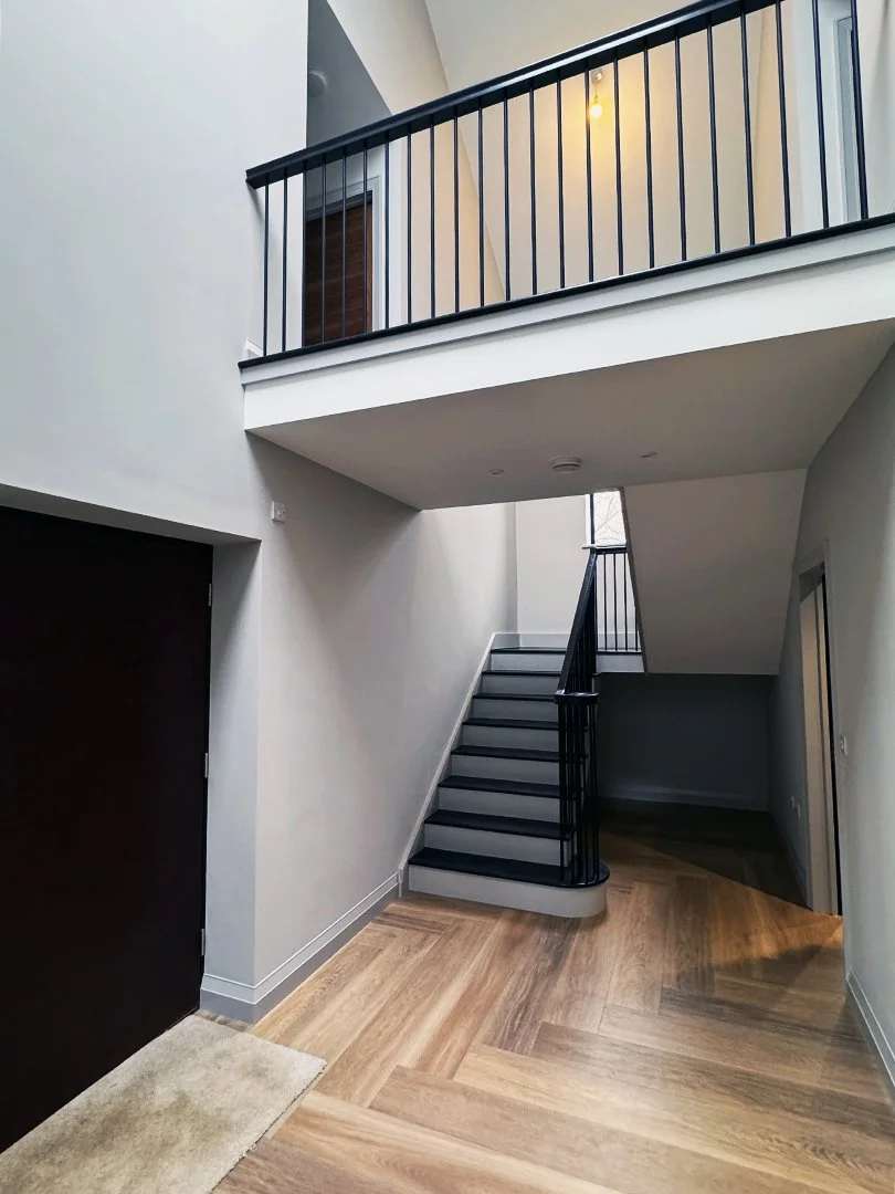 Interior view of a modern staircase with black railings, wooden flooring, and light gray walls in a residential home.
