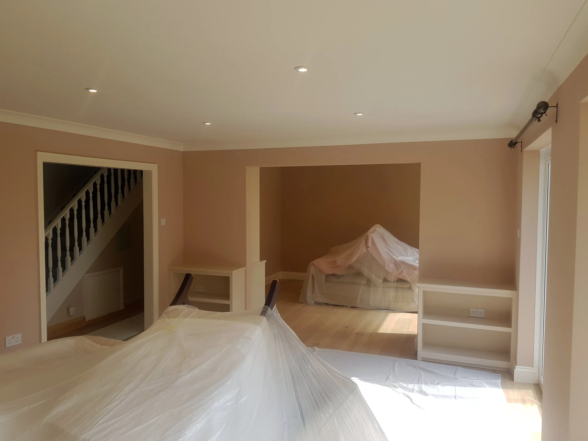 Living room with beige walls and wooden flooring, covered furniture, and ceiling lights.