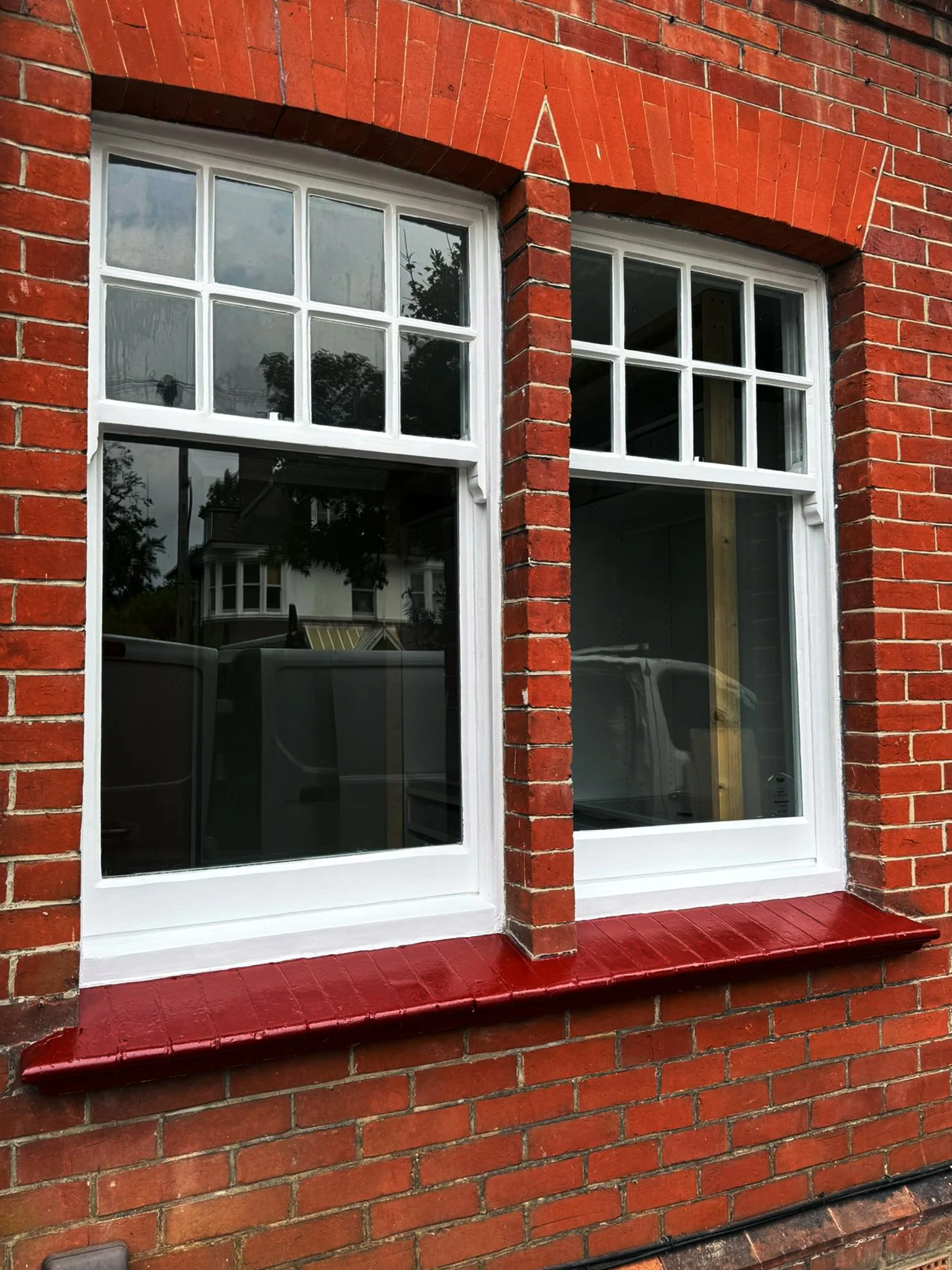 Close-up of two white-framed windows set in a red brick wall with a red brick sill below.