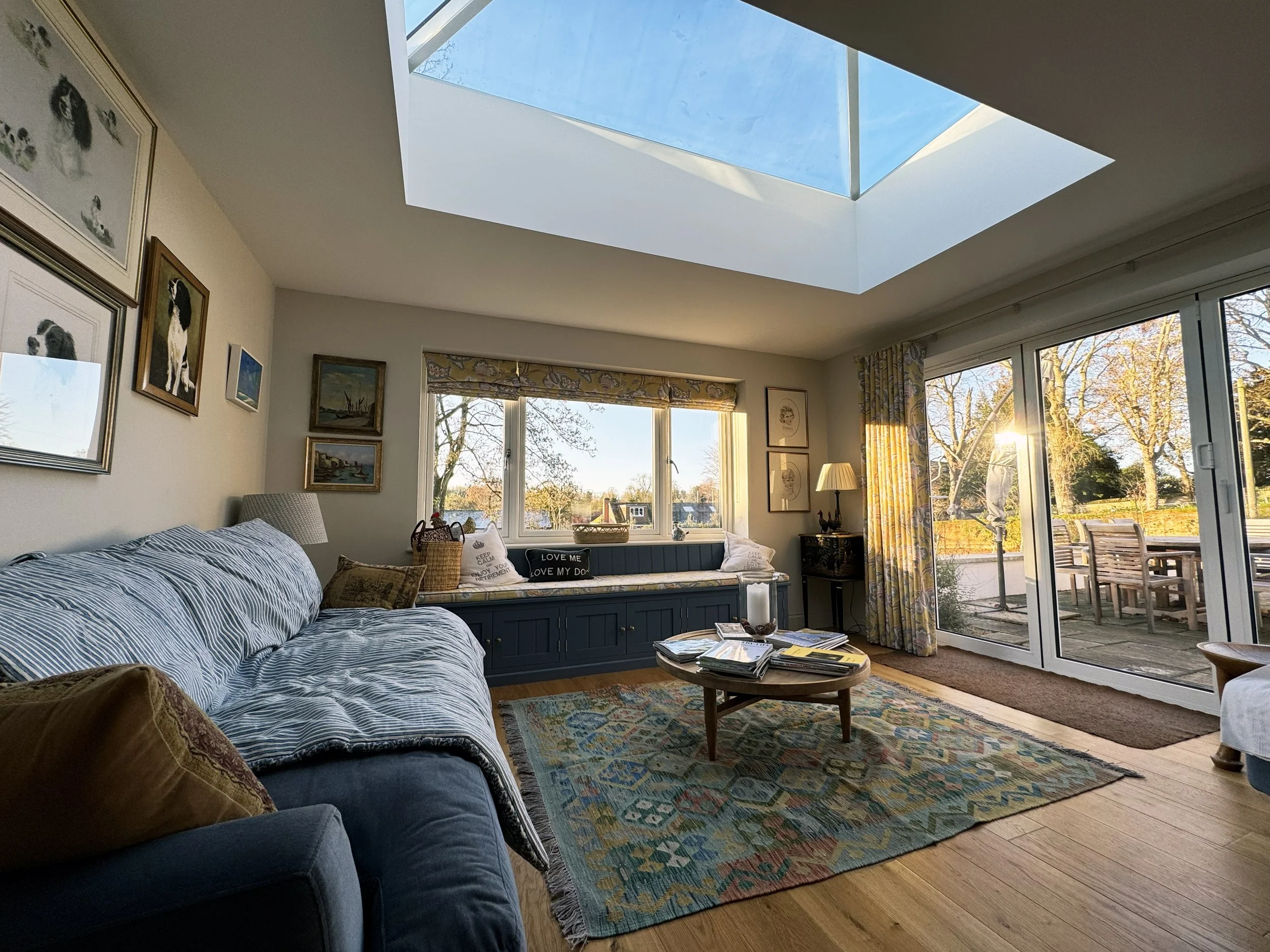 Living room with large skylight, sliding glass doors to outdoor patio, blue sofa, colorful rug, and framed pictures on the walls.