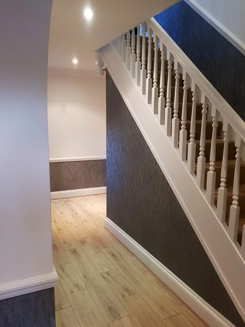 Interior hallway with staircase, white railing, dark textured wallpaper, and light wooden floor.
