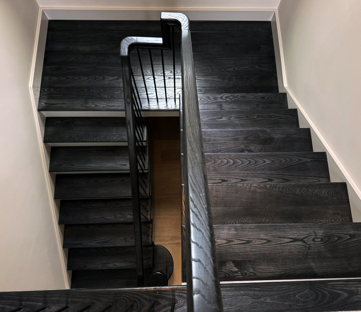 View of a dark wooden staircase from the top, looking down, with black metal handrails and white trim along the walls.