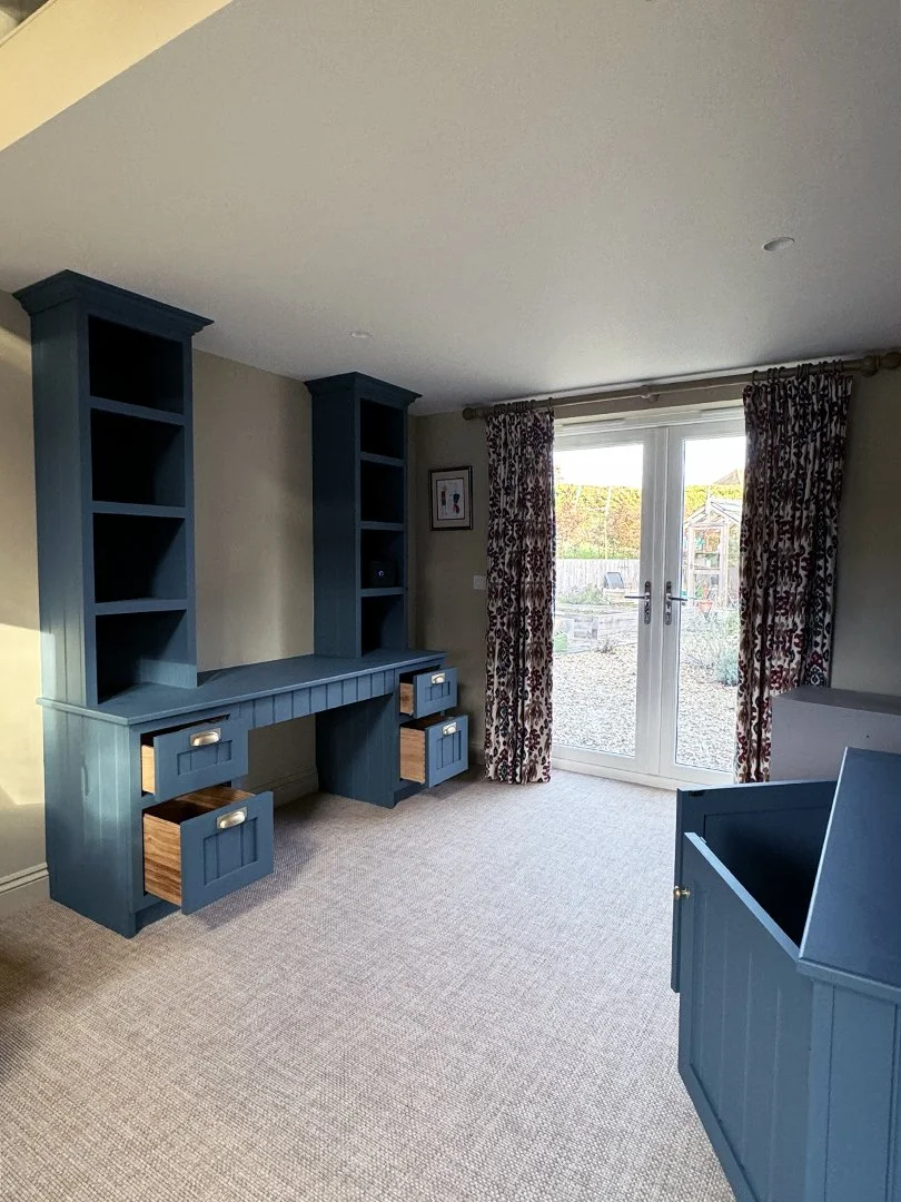 Empty room with built-in blue shelves and drawers, beige carpet, and glass doors with floral curtains leading outside.