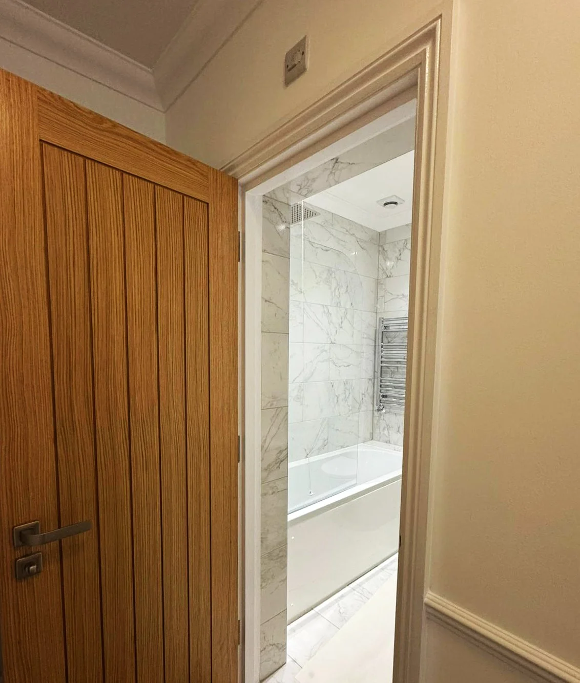Open bathroom door revealing a marble-tiled shower with a glass partition and a heated towel rail.
