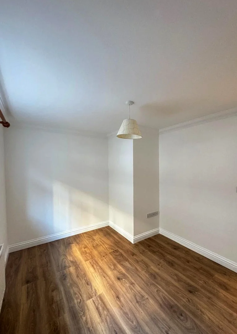 Empty room with white walls, hardwood flooring, and a ceiling light fixture.