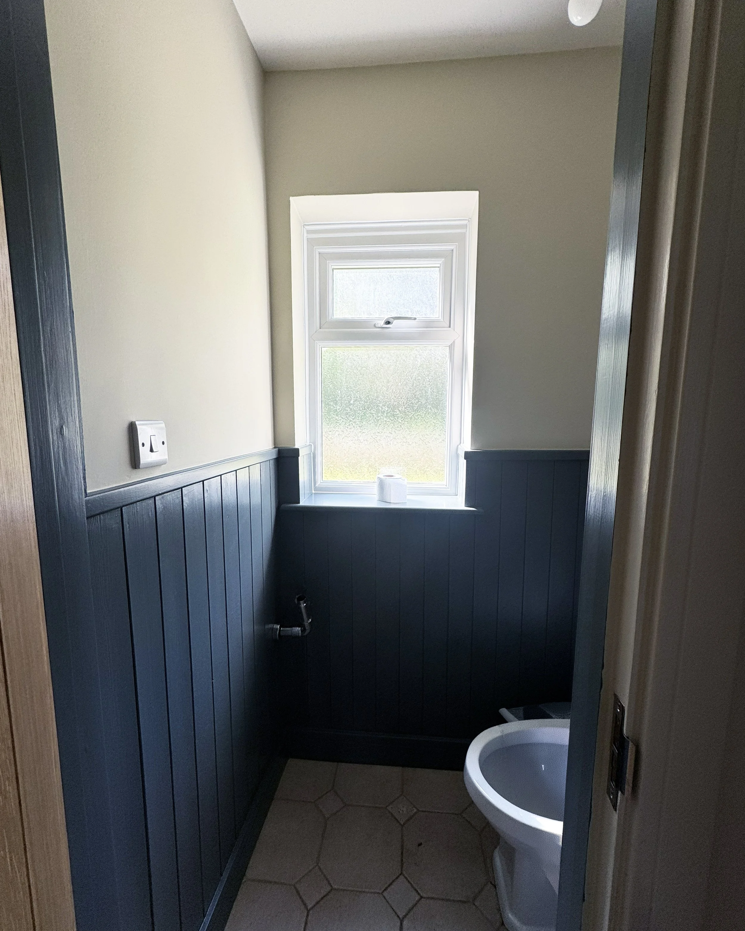 Small bathroom with a frosted window, beige walls with blue wainscoting, and a white toilet.
