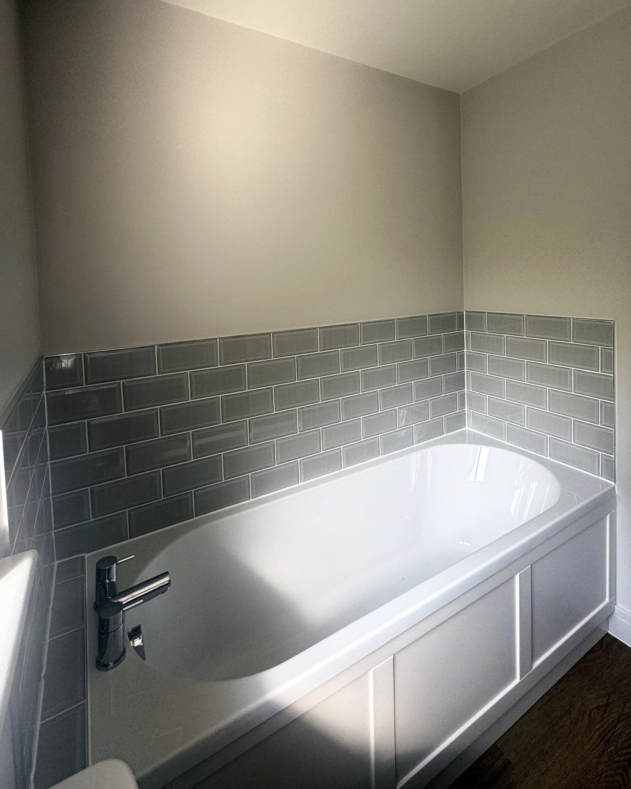 White bathtub with dark gray tile backsplash in a bathroom.