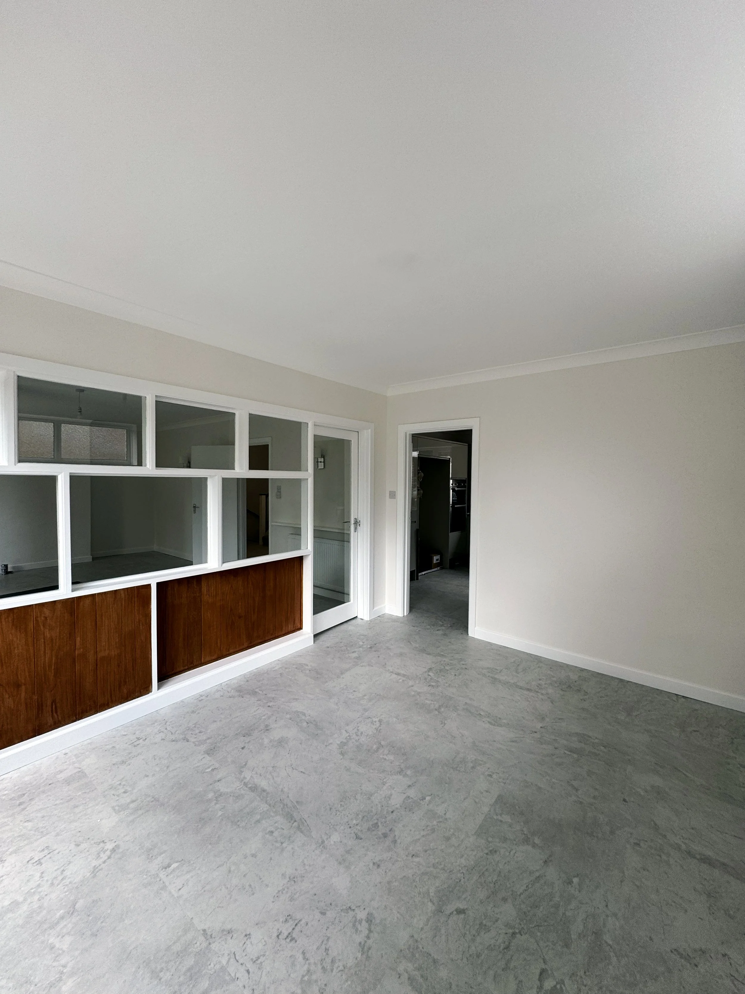 Empty living room with gray flooring, white walls, a built-in wood panel and a glass door leading to another room.