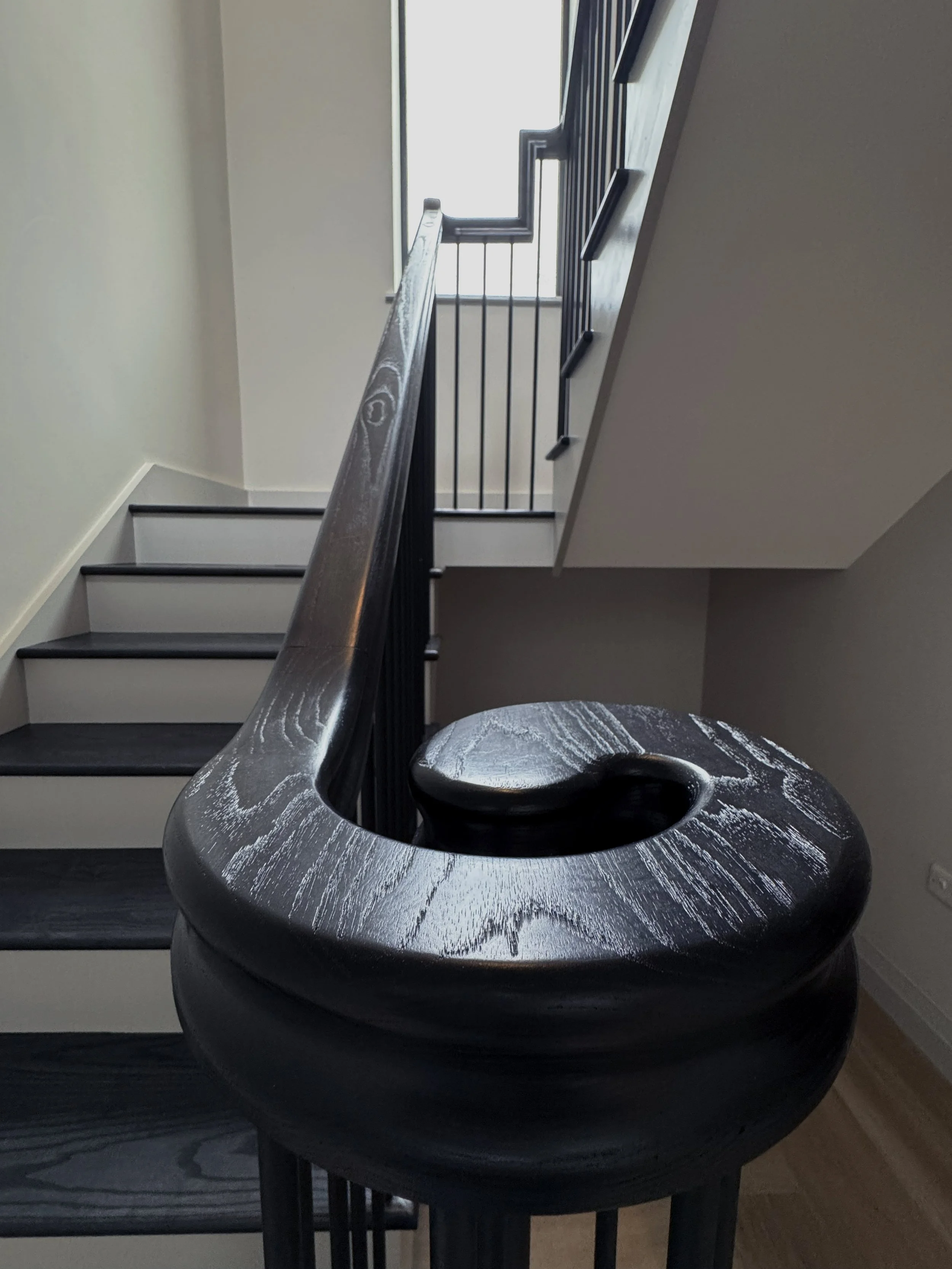 Close-up of a black wooden spiral staircase handrail and the top of a newel post.
