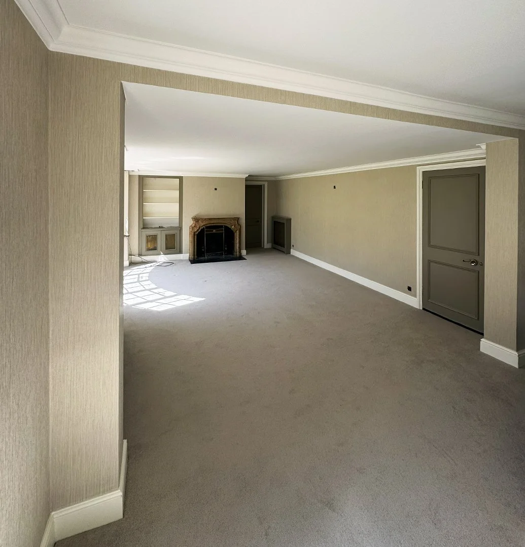 Empty living room with beige walls, a fireplace, built-in shelves, and carpeted floors.