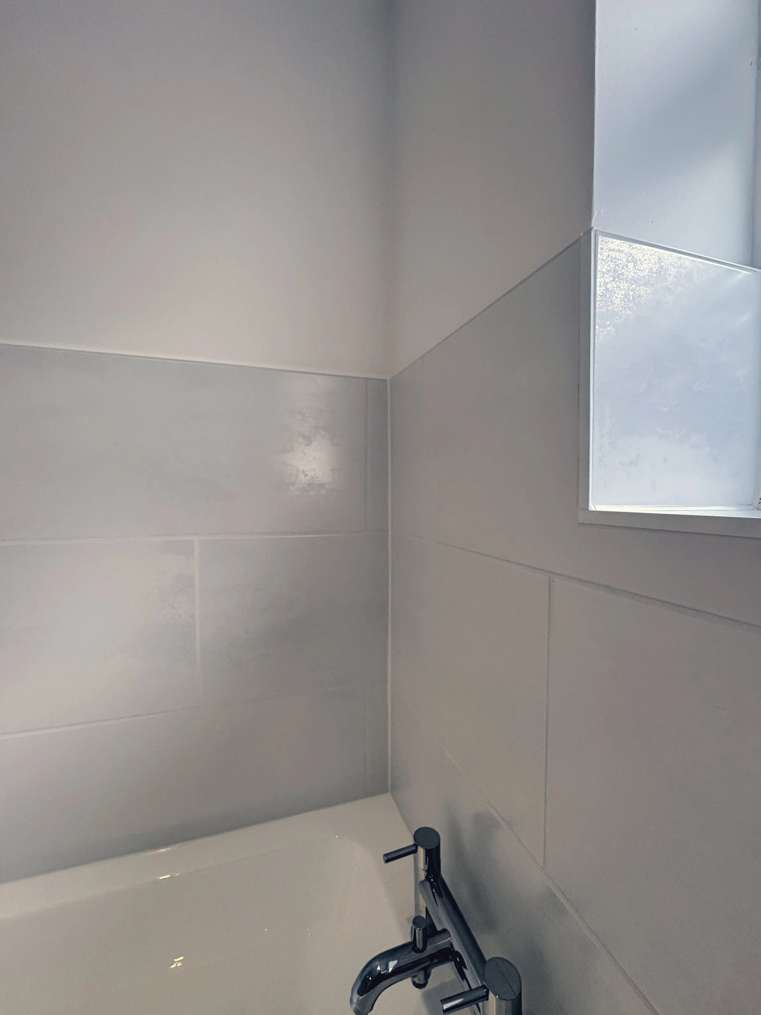 A bathroom corner with a white bathtub, chrome faucet, white wall tiles, and a small frosted window.