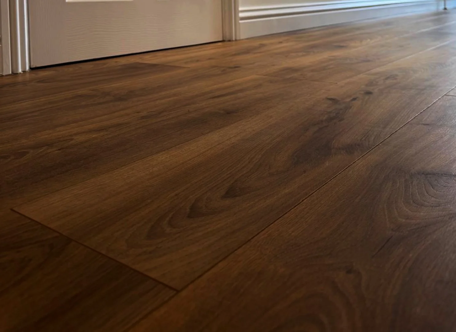 Close-up view of a wooden floor near a door, showing the natural grain and texture of the dark brown wood.
