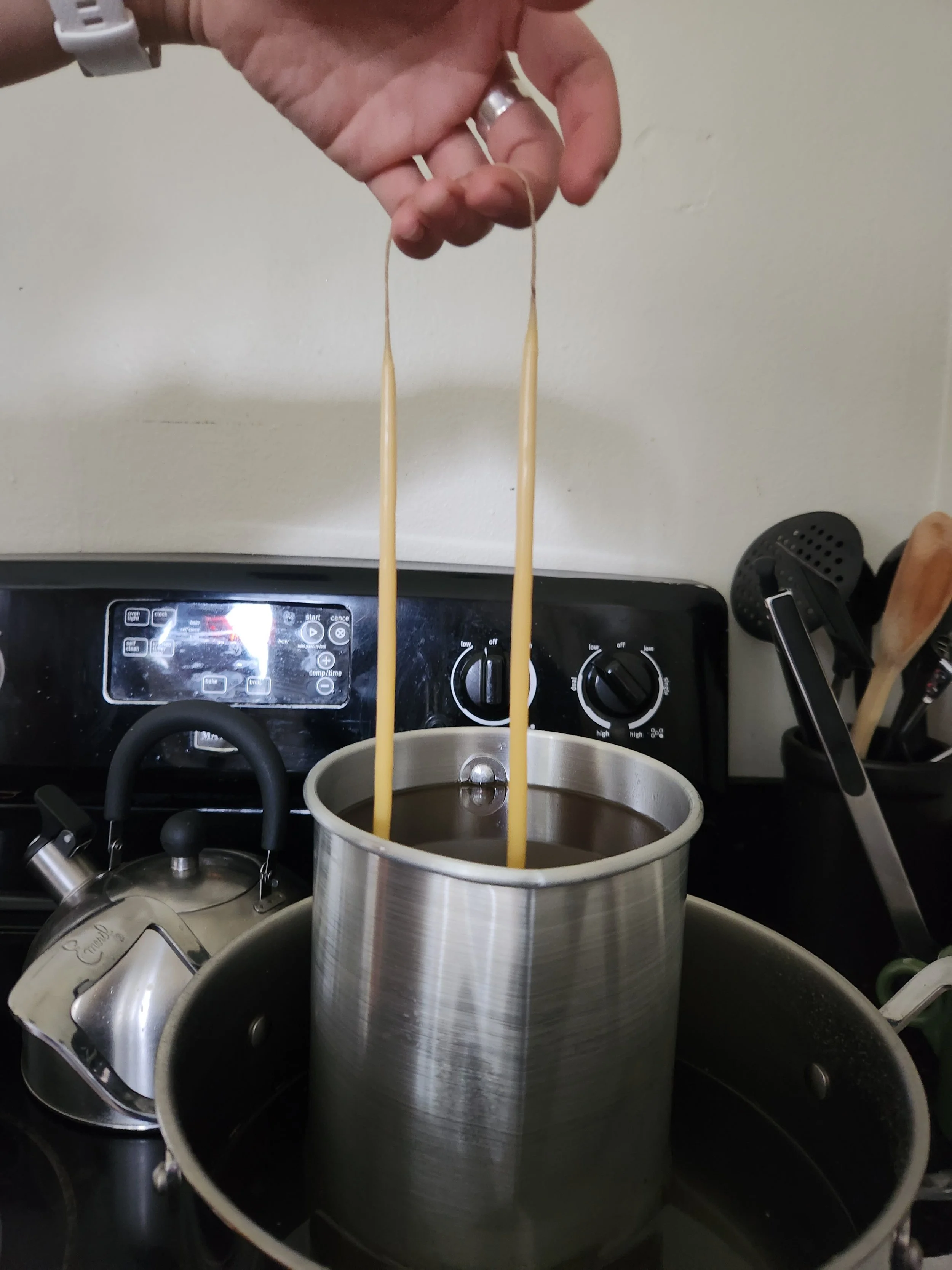 a hand is seen dipping candles into a pot of wax on a stove top