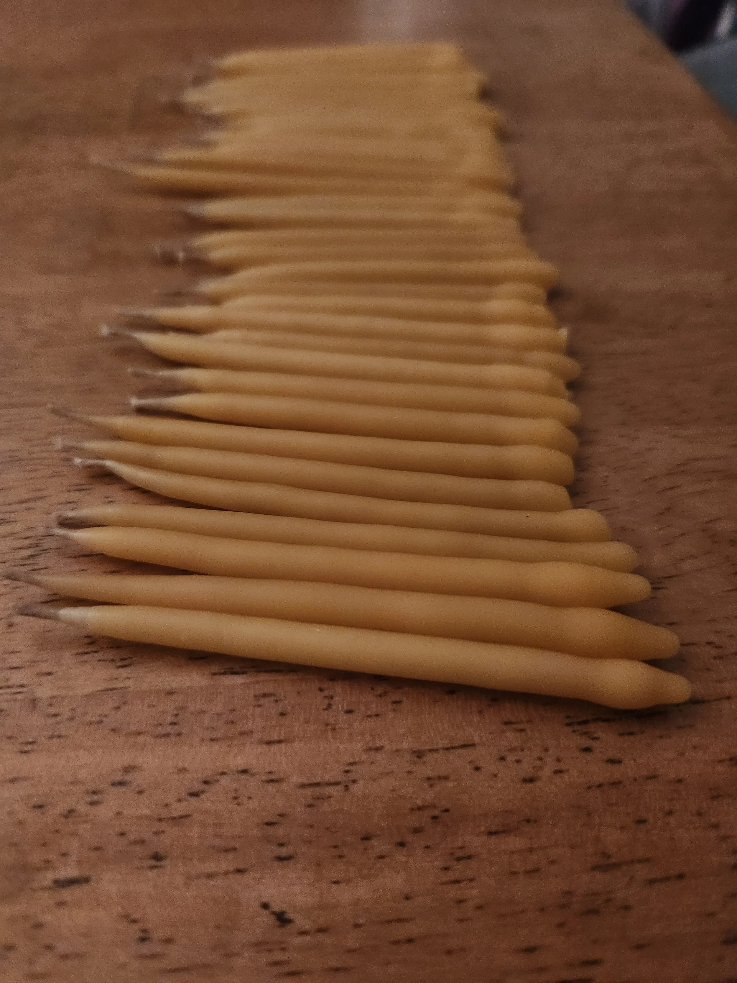 a neatly arranged row of hand-dipped birthday candles is shown. they are laying on a wood surface. the foreground shows the first candle up close and then the row of candles recedes into the distance of the photo.