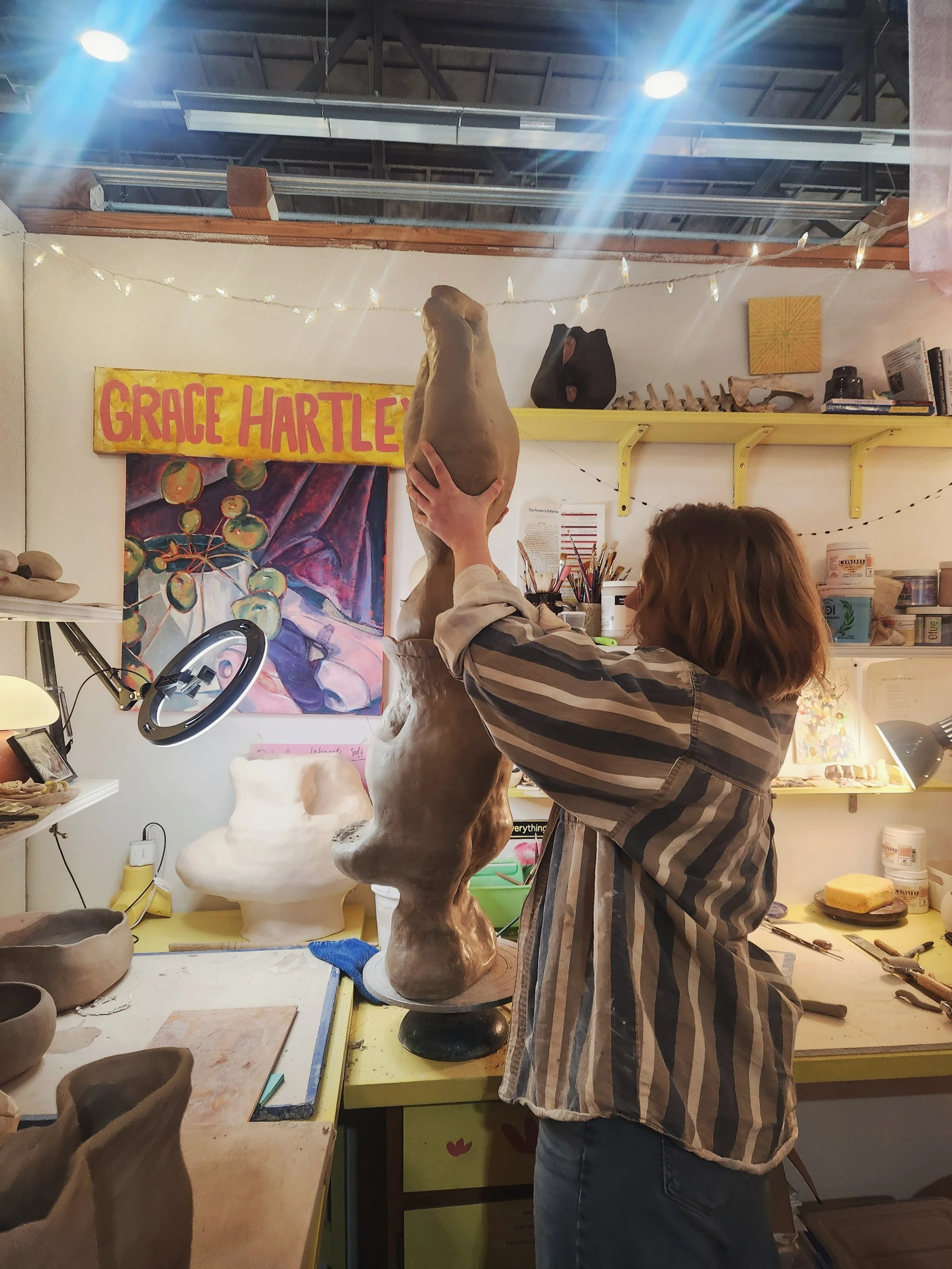 Grace Hartley in her studio, stacking a clay sculpture as tall as her
