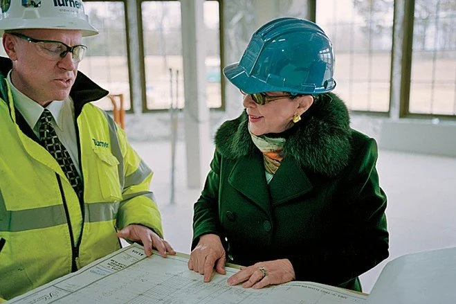 A man and woman in hard hats examining construction plans at a worksite.