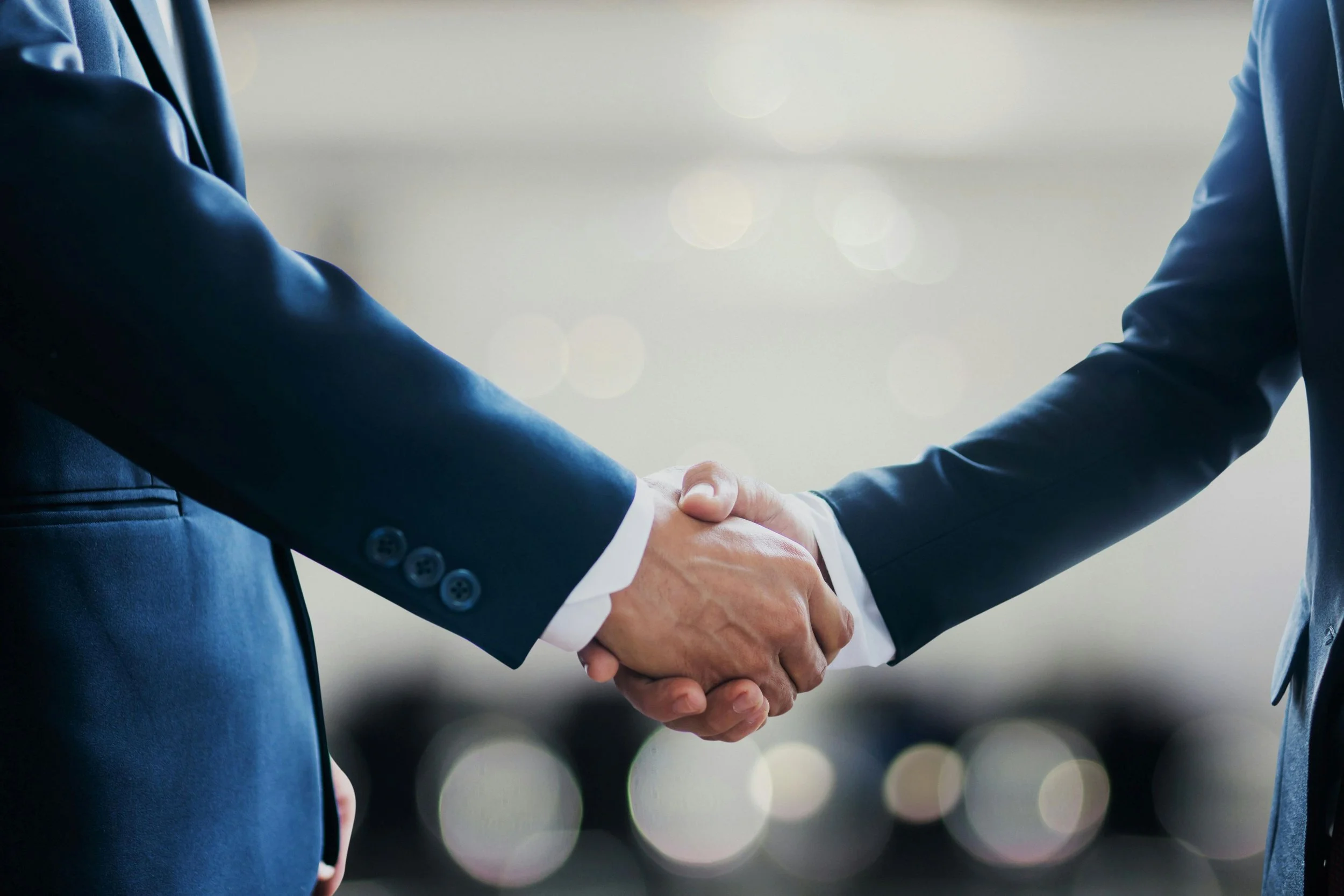 Two business professionals shaking hands, with a blurred background suggesting a corporate environment.