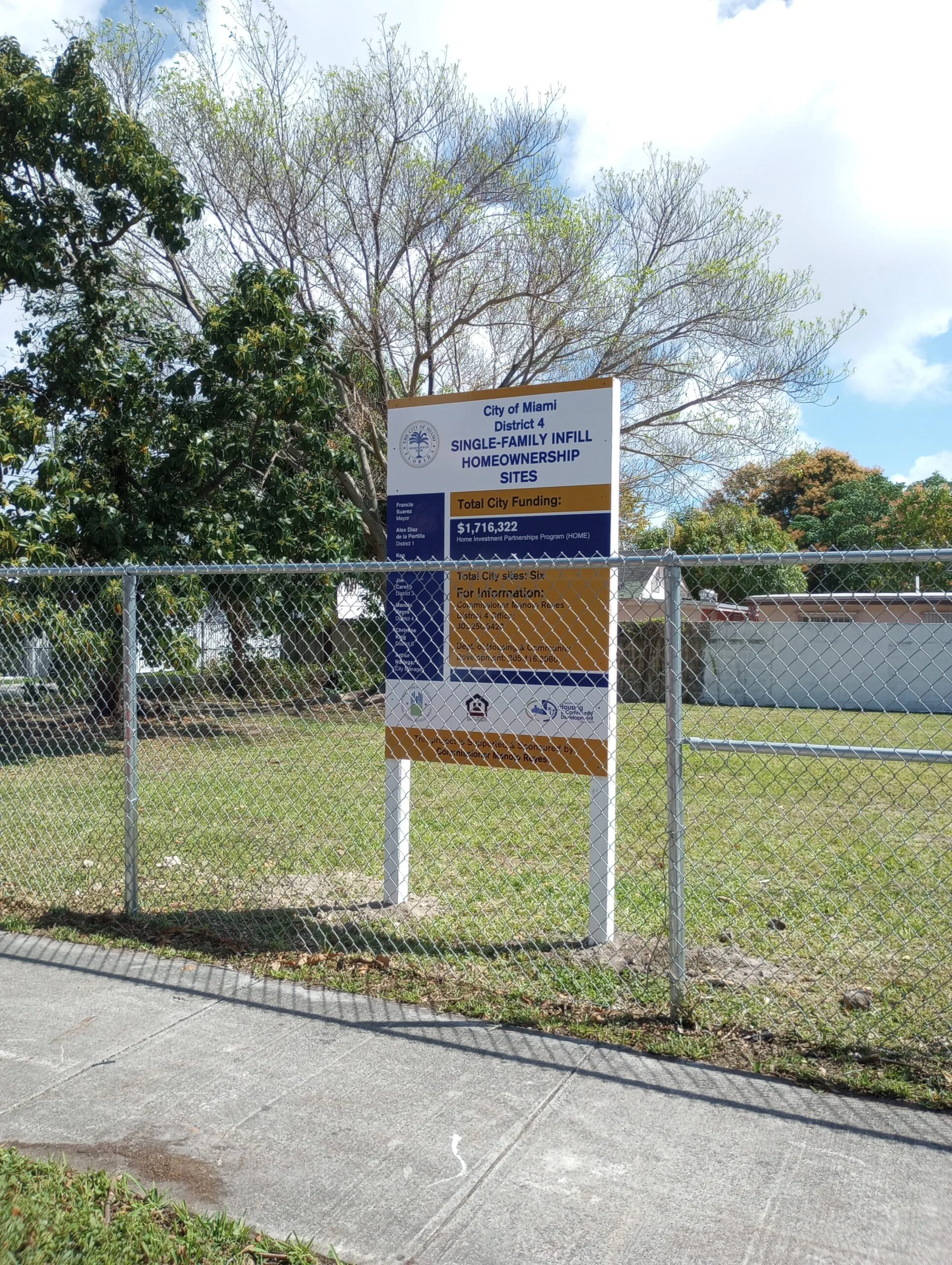 A sign on a fence in front of a grassy area, indicating rules or information about the space.