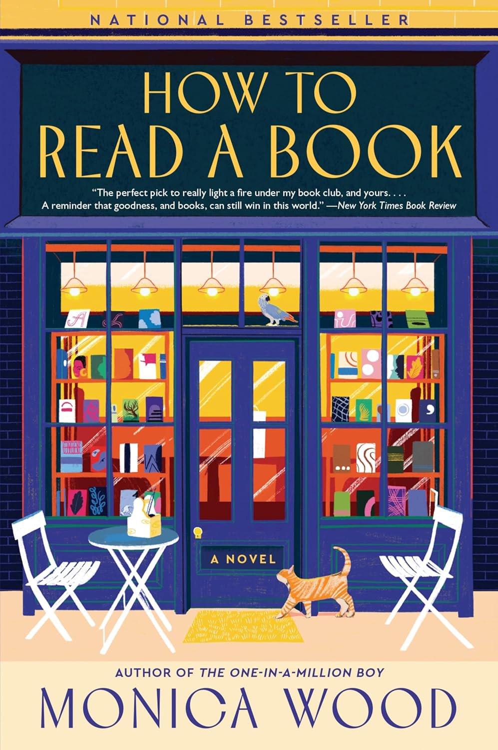 A bookstore with large front windows displaying books, a sign above that reads 'How to Read a Book,' and a quote from a New York Times review. The store has a blue exterior and yellow accents, with two white chairs and a small table outside. A cat is near the door, and a bird is sitting on the window ledge.
