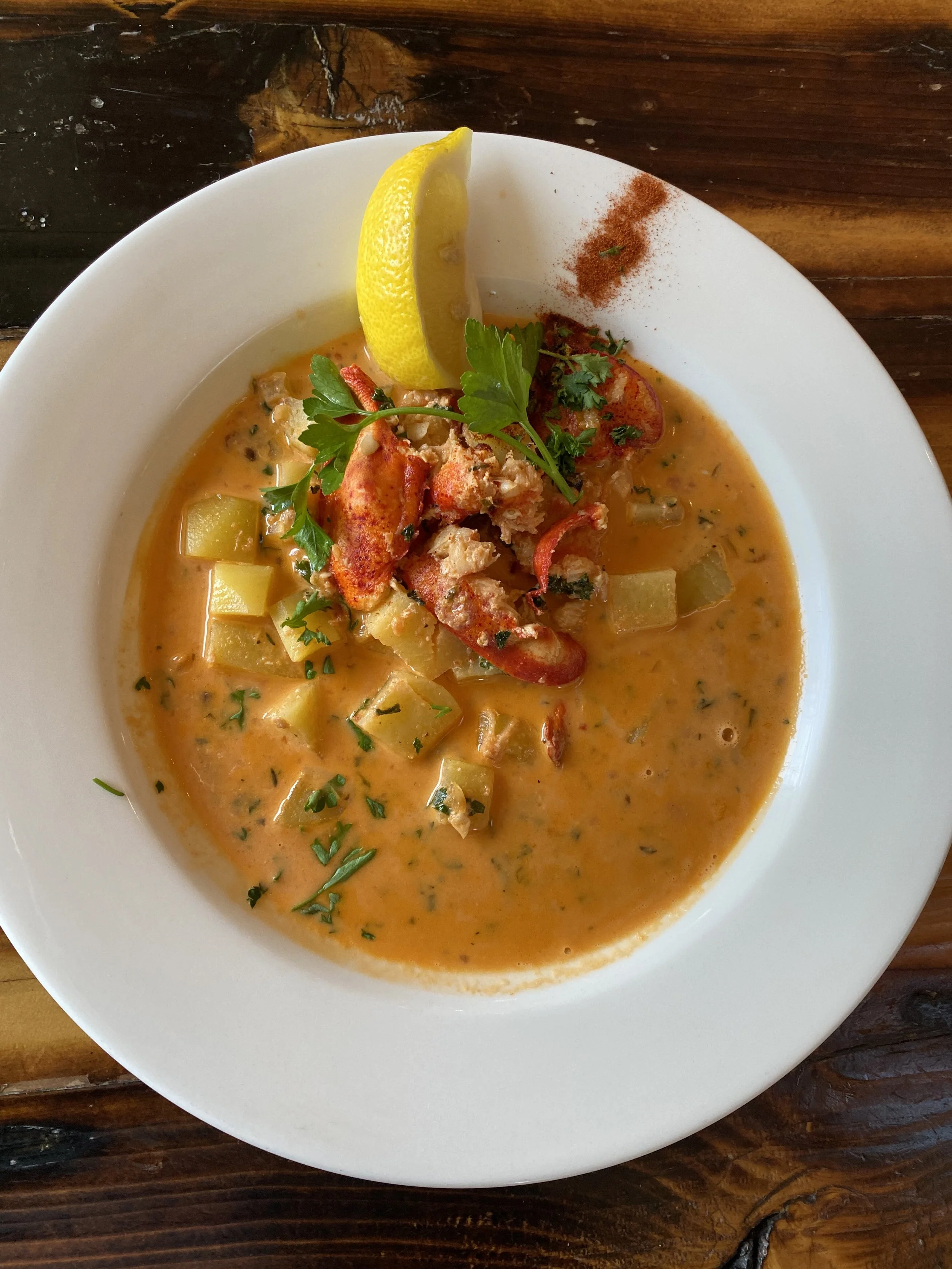 Bowl of seafood soup garnished with cilantro, served with a lemon wedge and chili powder on a white plate.