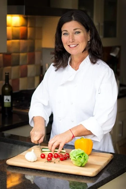 Chef Hana in a white chef's coat chopping vegetables on a wooden cutting board in a kitchen.