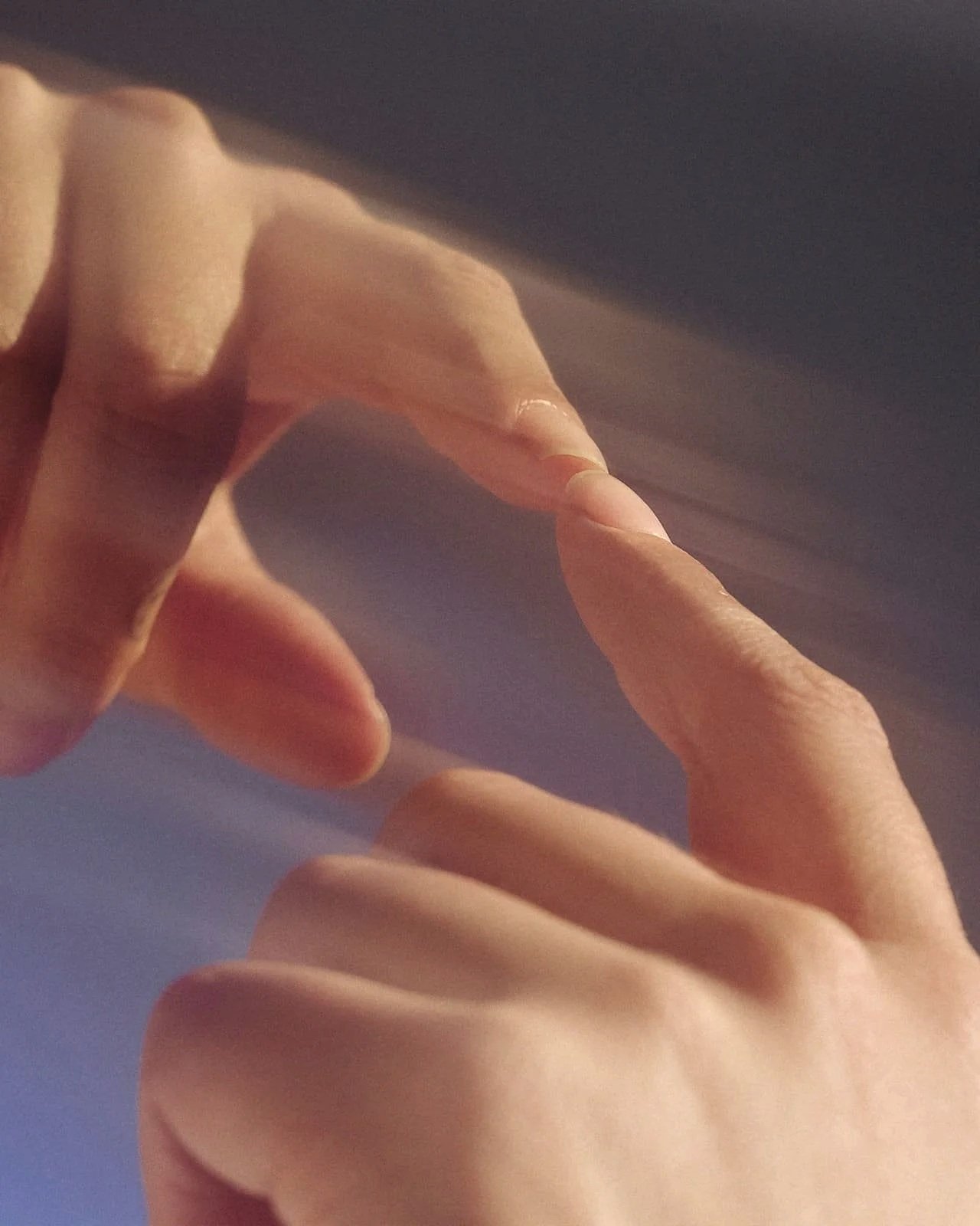 Close-up of two hands with fingers extended, touching each other against a blue background.