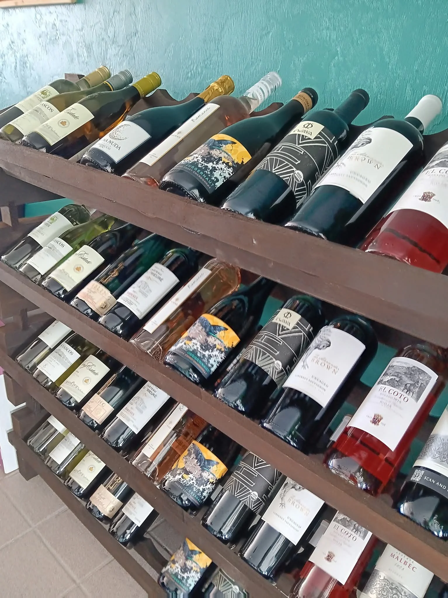 View of multiple shelves with various bottles of wine in a store, arranged horizontally and angled, with labels of different designs and colors.