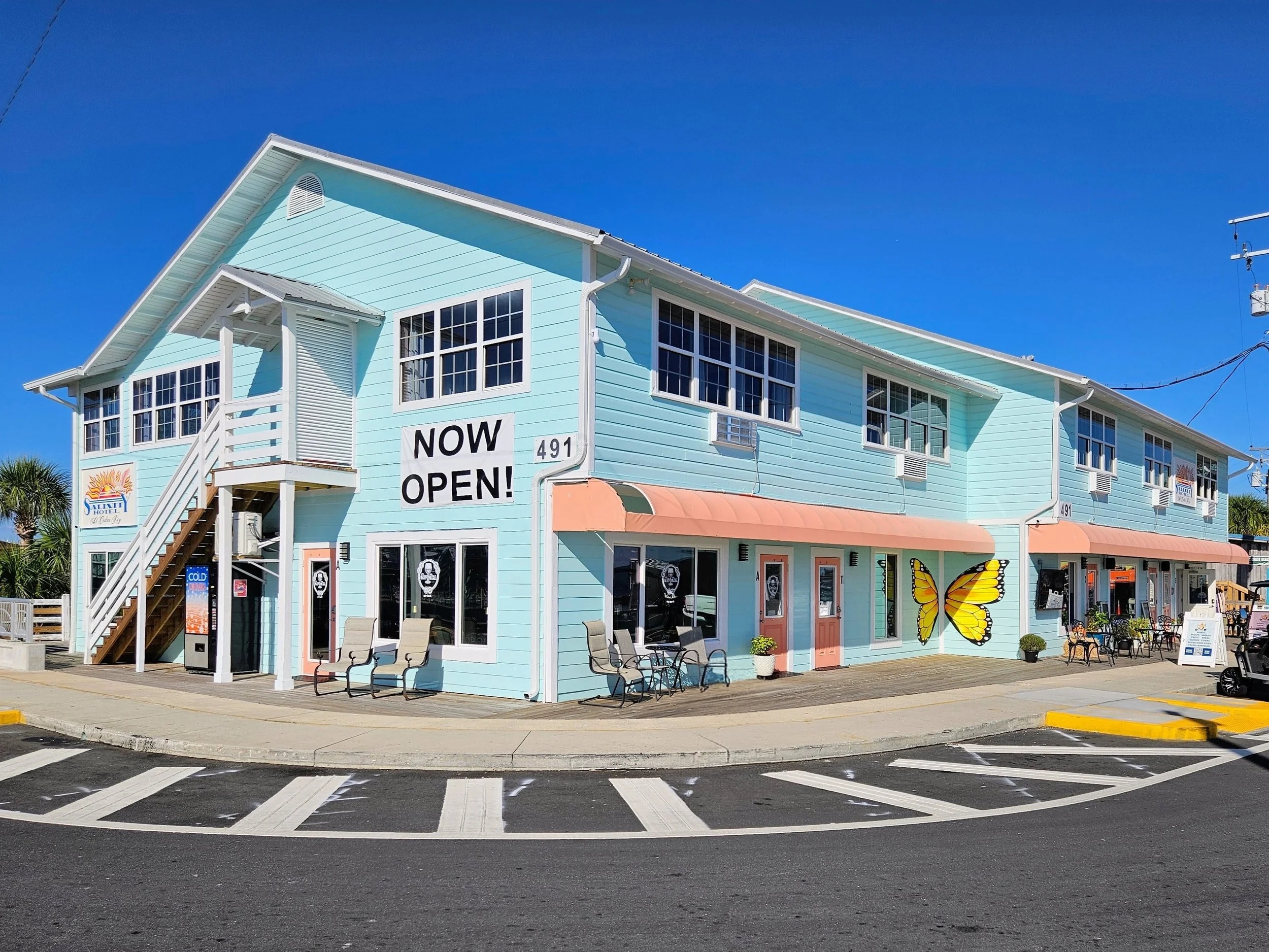 Light blue two-story building with an upstairs staircase, large windows, orange awnings, and a butterfly mural on the side, indicating a newly opened business.
