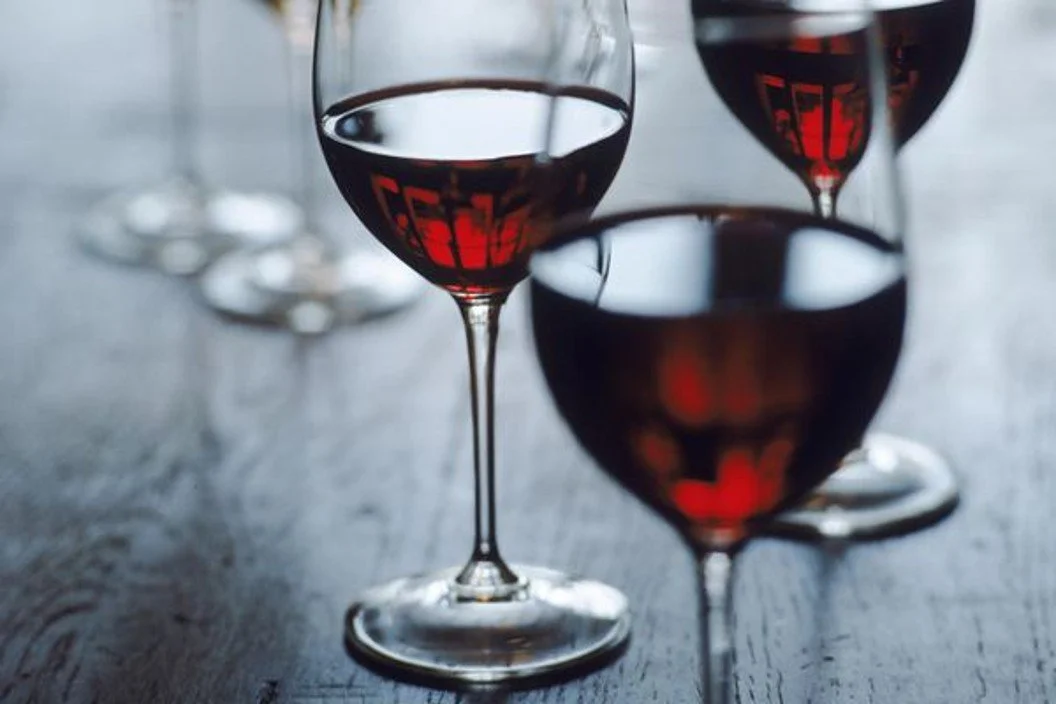 Three glasses of red wine on a dark wooden table, with reflections and a blurred background.