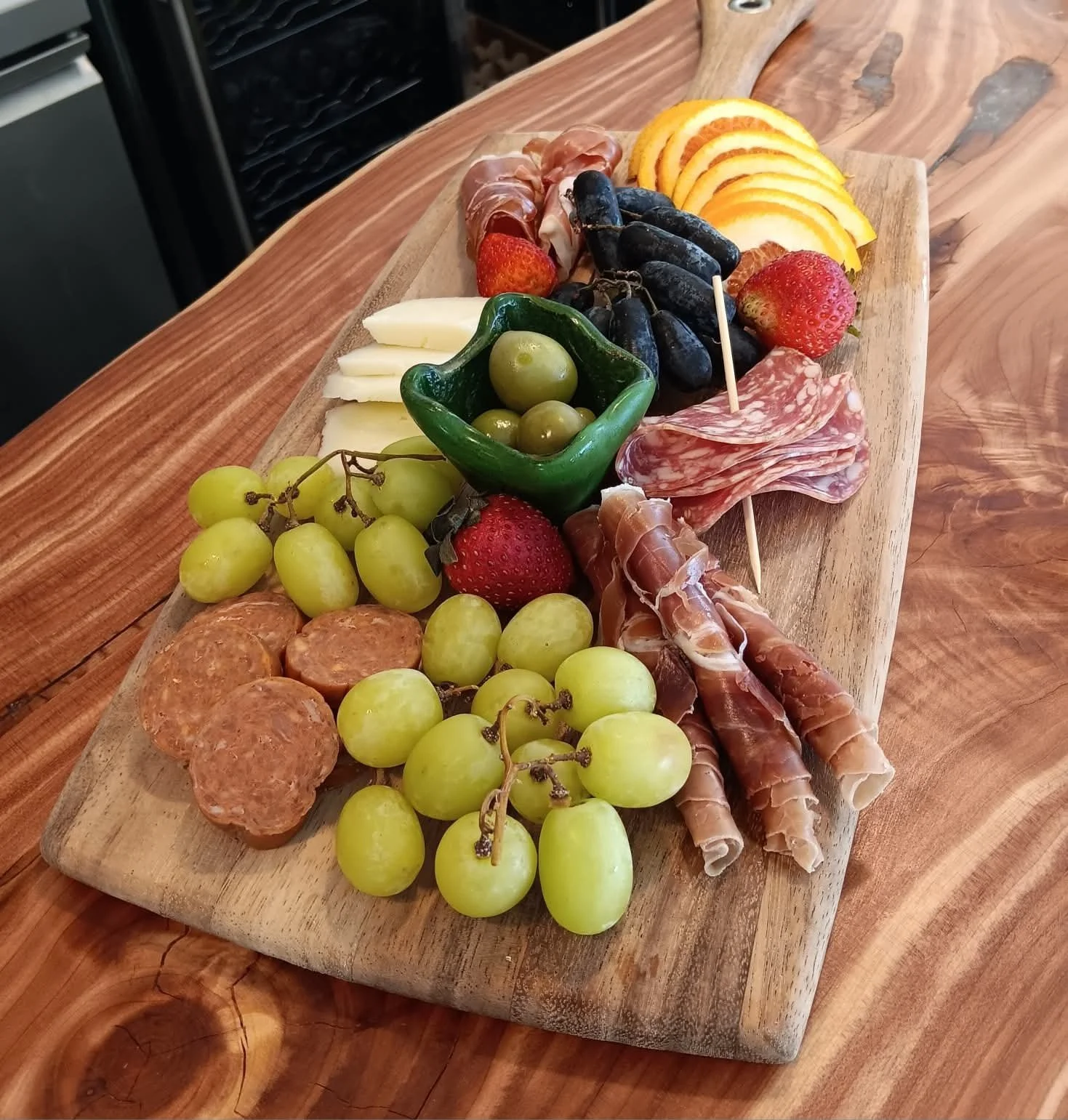 Charcuterie board with grapes, strawberries, cheese, cured meats, olives, and sliced fruit on a wooden table.
