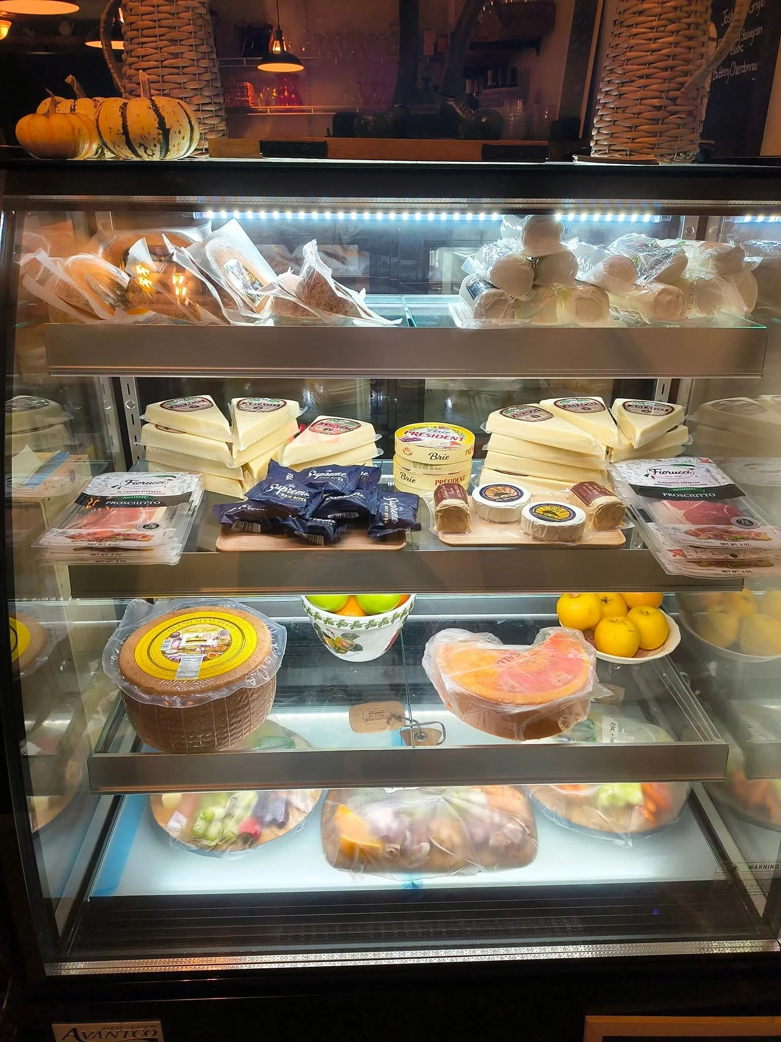 Display case with cheeses, meats, pumpkins, and fruits.