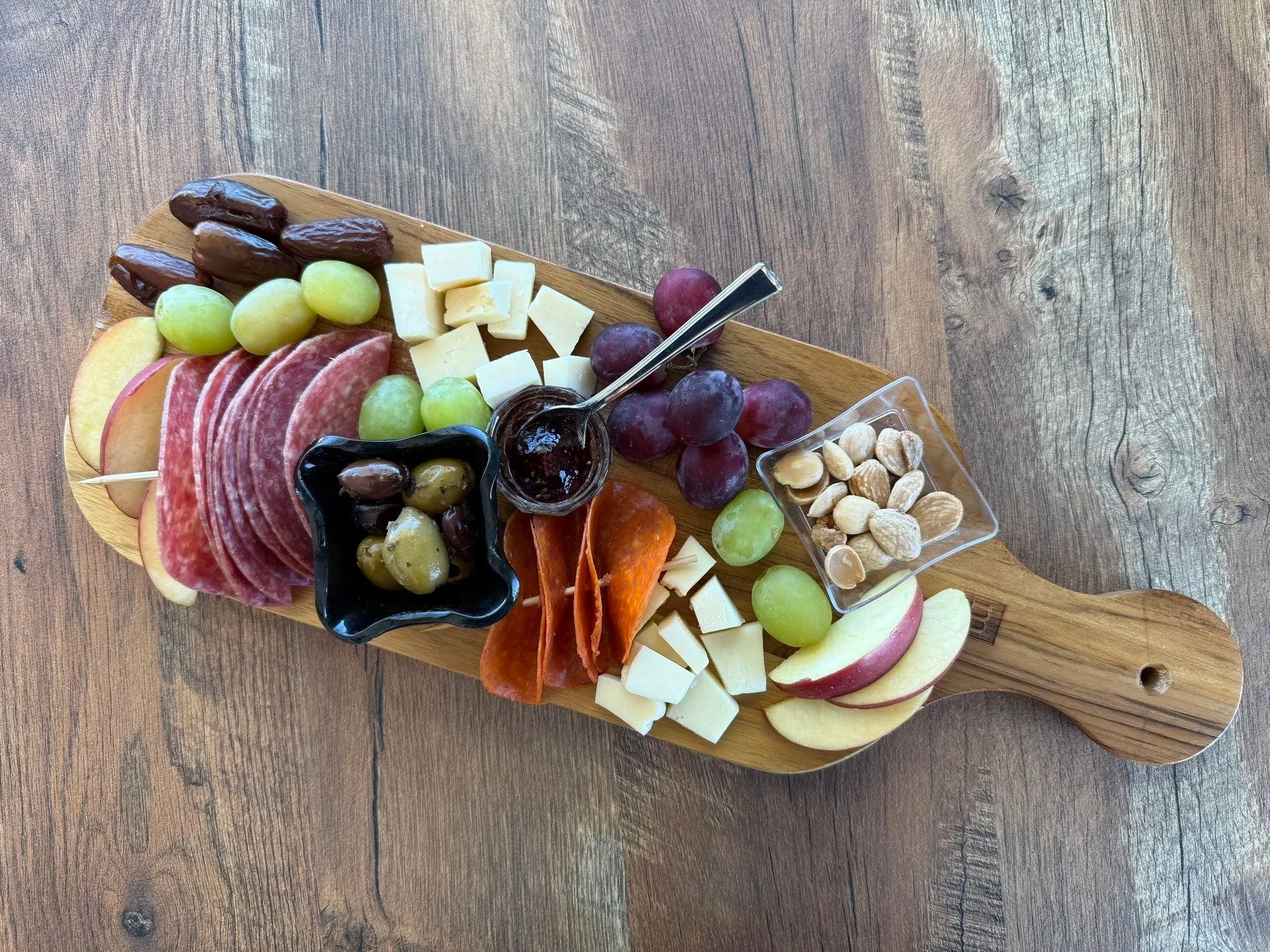 Wooden charcuterie board with an assortment of cheese, cured meats, olives, nuts, fruit and compote.