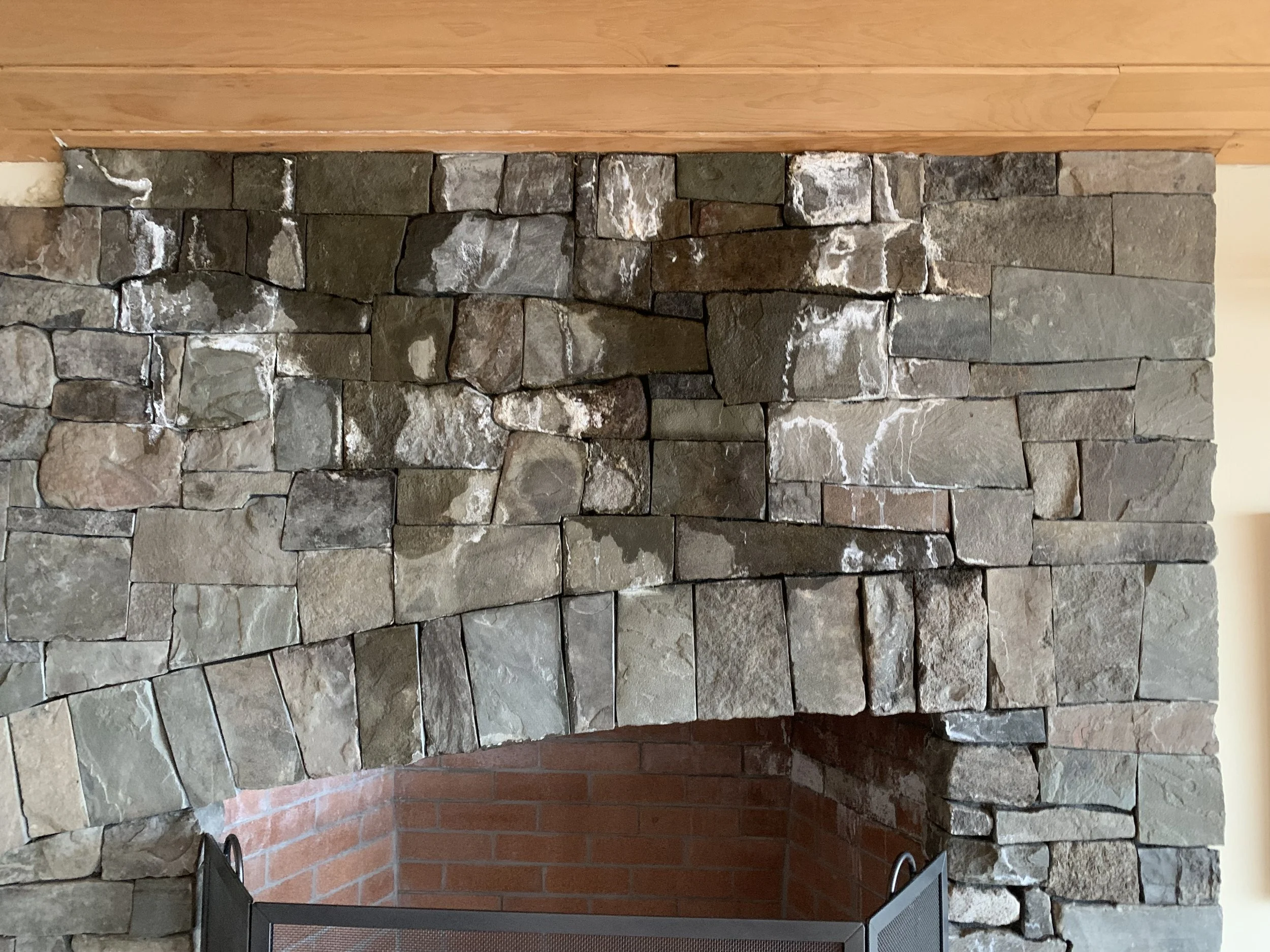 A stone fireplace with a rounded opening, topped by a wooden mantel and a water leak seeping through the stone.