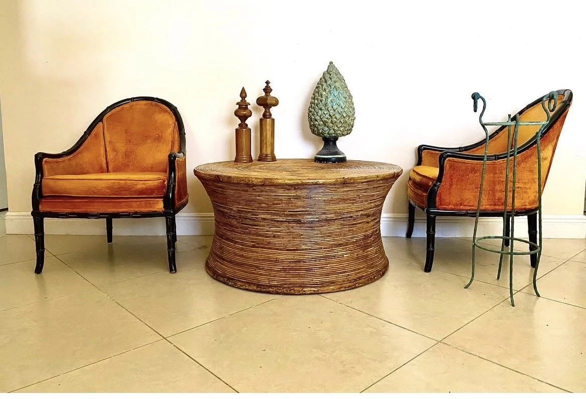 Two vintage orange armchairs with dark wooden frames flanking a round wooden table with decorative objects on top, against a plain white wall and tiled floor.