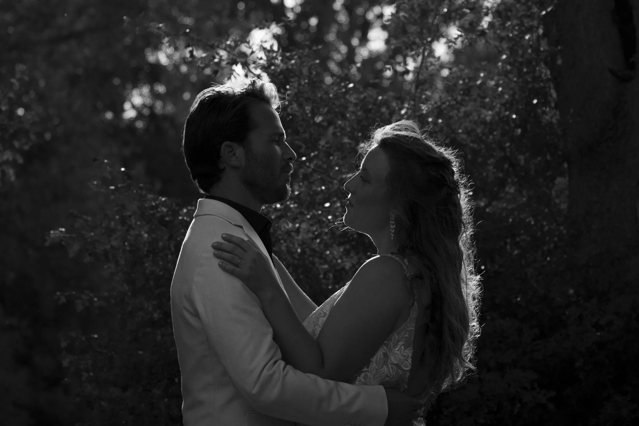 Un couple danse dans la nature, l'homme porte un costume blanc et la femme une robe élégante. La scène est en noir et blanc, entourée d'arbres.