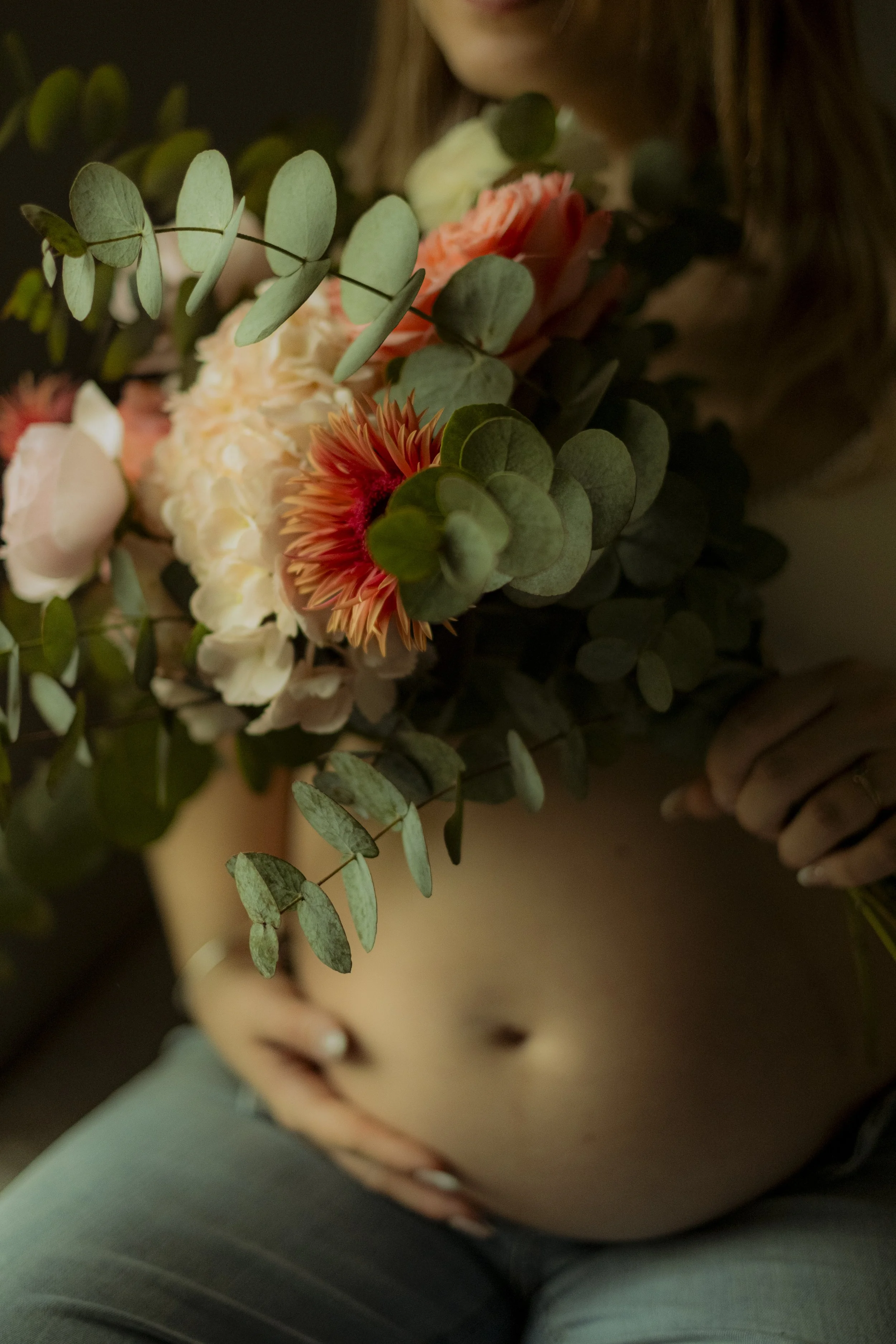 Une personne tenant un bouquet de fleurs comprenant des fleurs roses, des fleurs crème, des feuillages verts, avec un fond sombre.
