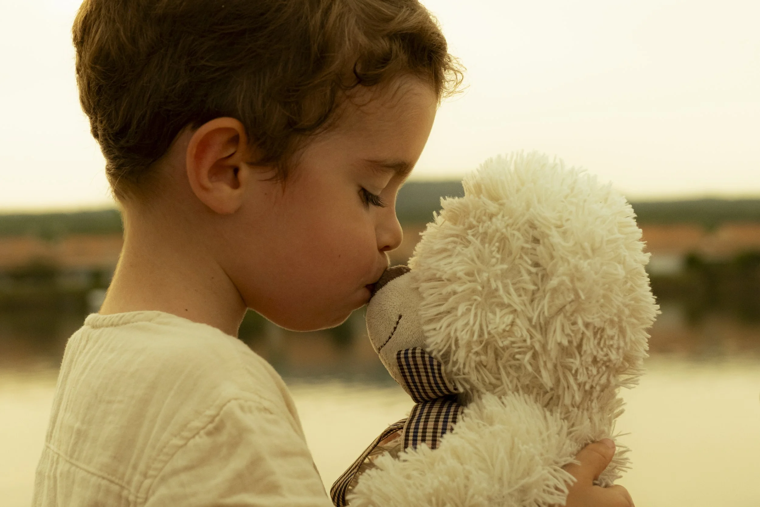 Un enfant avec les yeux fermés, tenant un jouet en peluche beige.