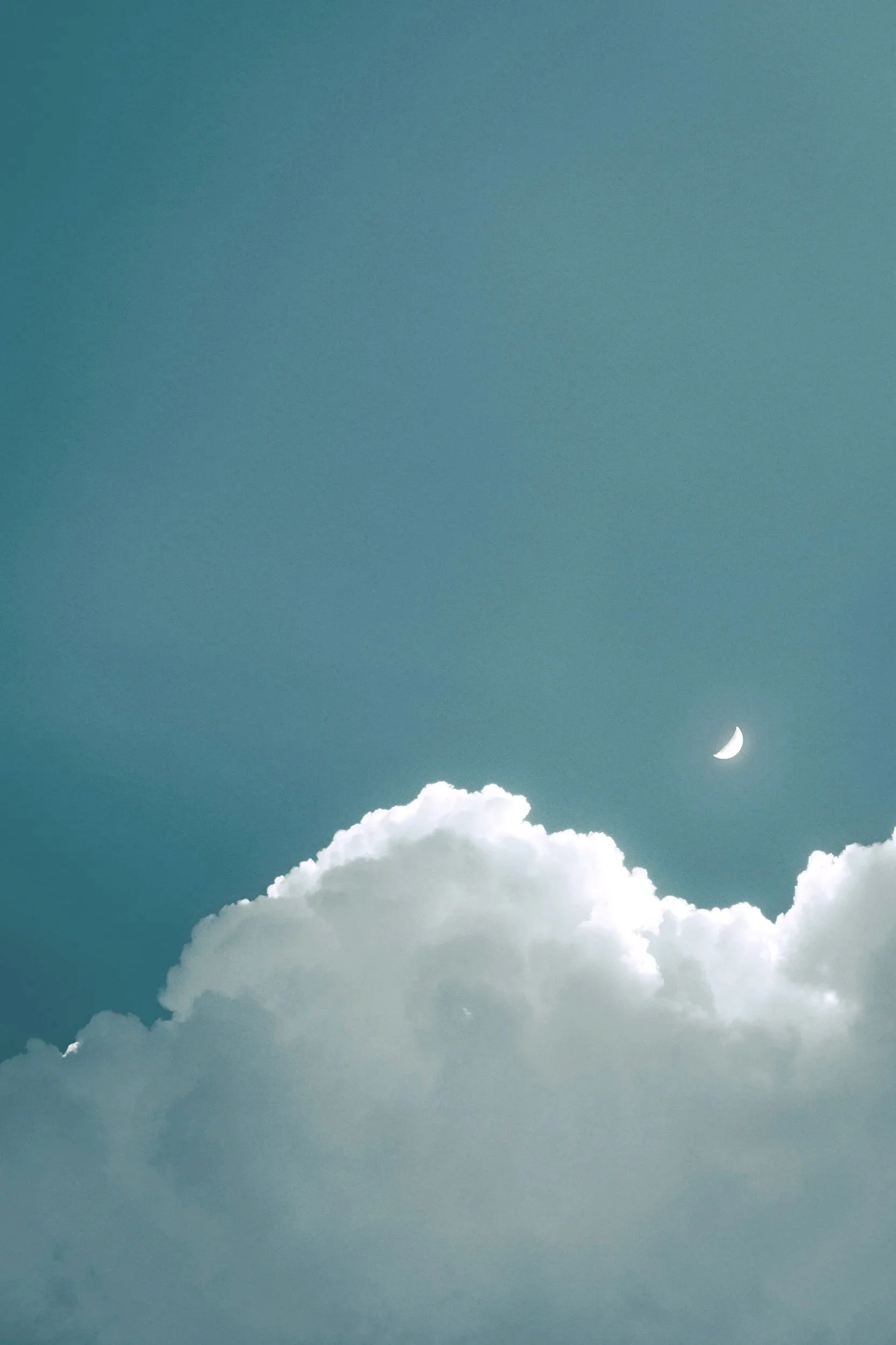 White cumulus clouds beneath a crescent moon in a blue sky