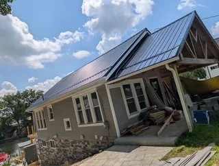 A house with a metal roof, tilted and leaning to one side, under construction or repair, with a boat stored underneath the patio area.