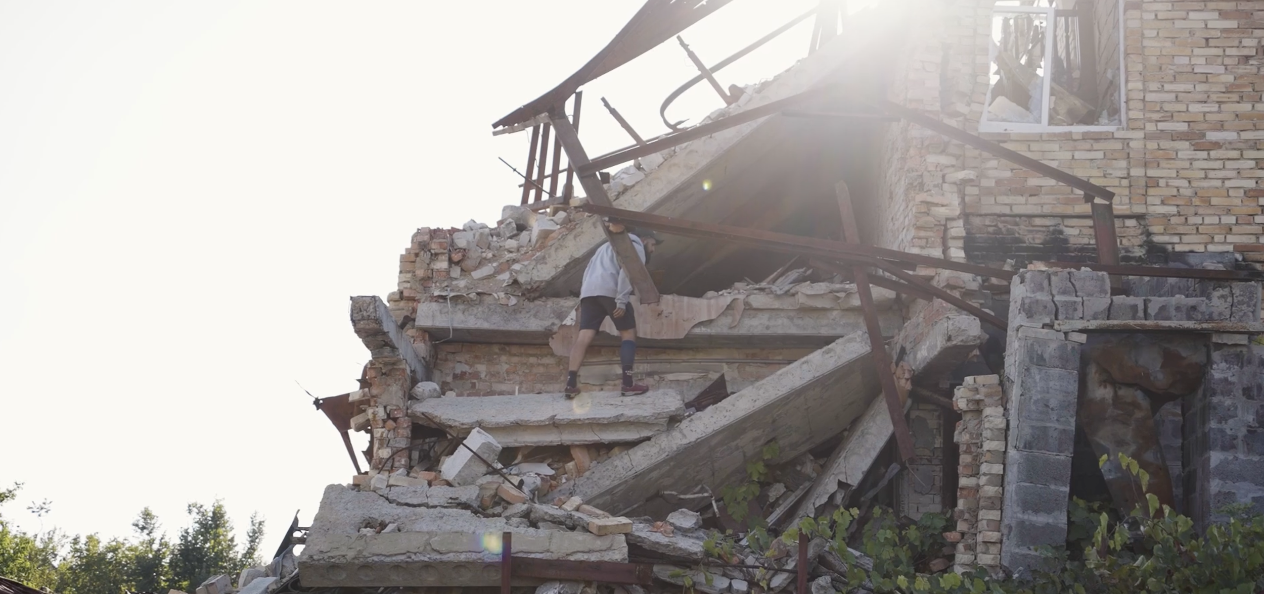 A person with a prosthetic leg exploring the ruins of a collapsed brick building in sunlight.